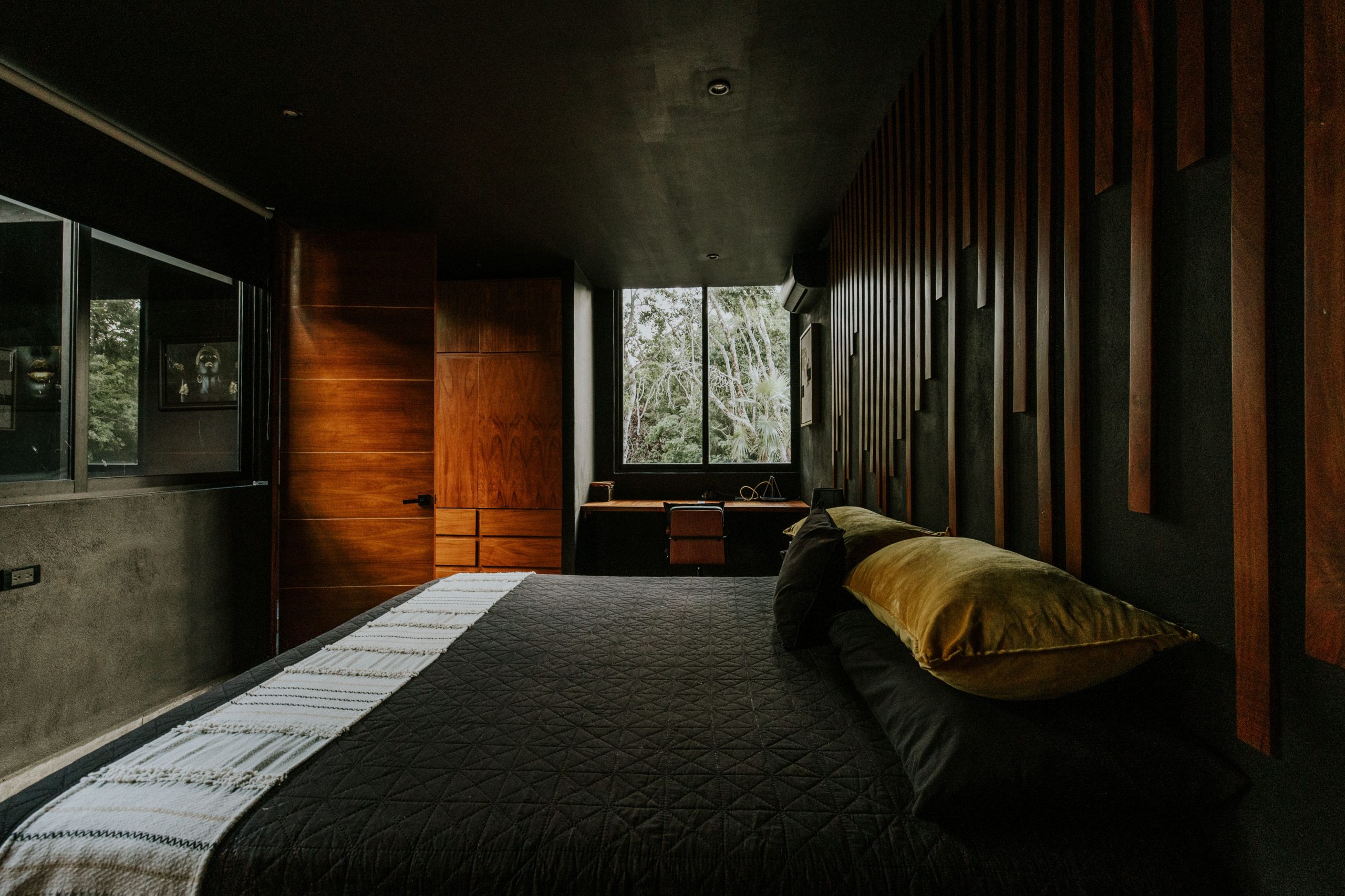 Contemporary bedroom with dark tones, wood accents, and a large window view.