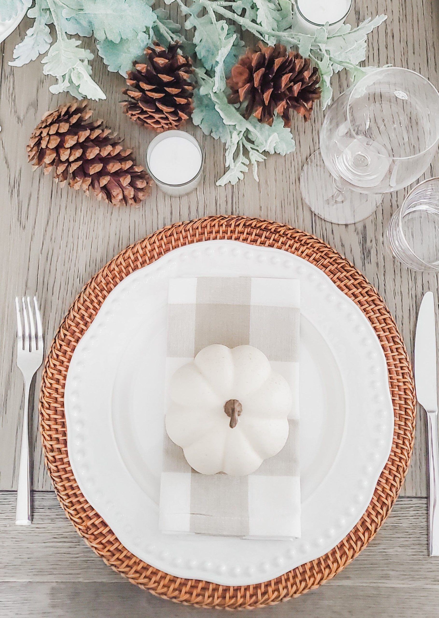 Cozy fall table decor featuring a white pumpkin, pinecones, and elegant place settings.
