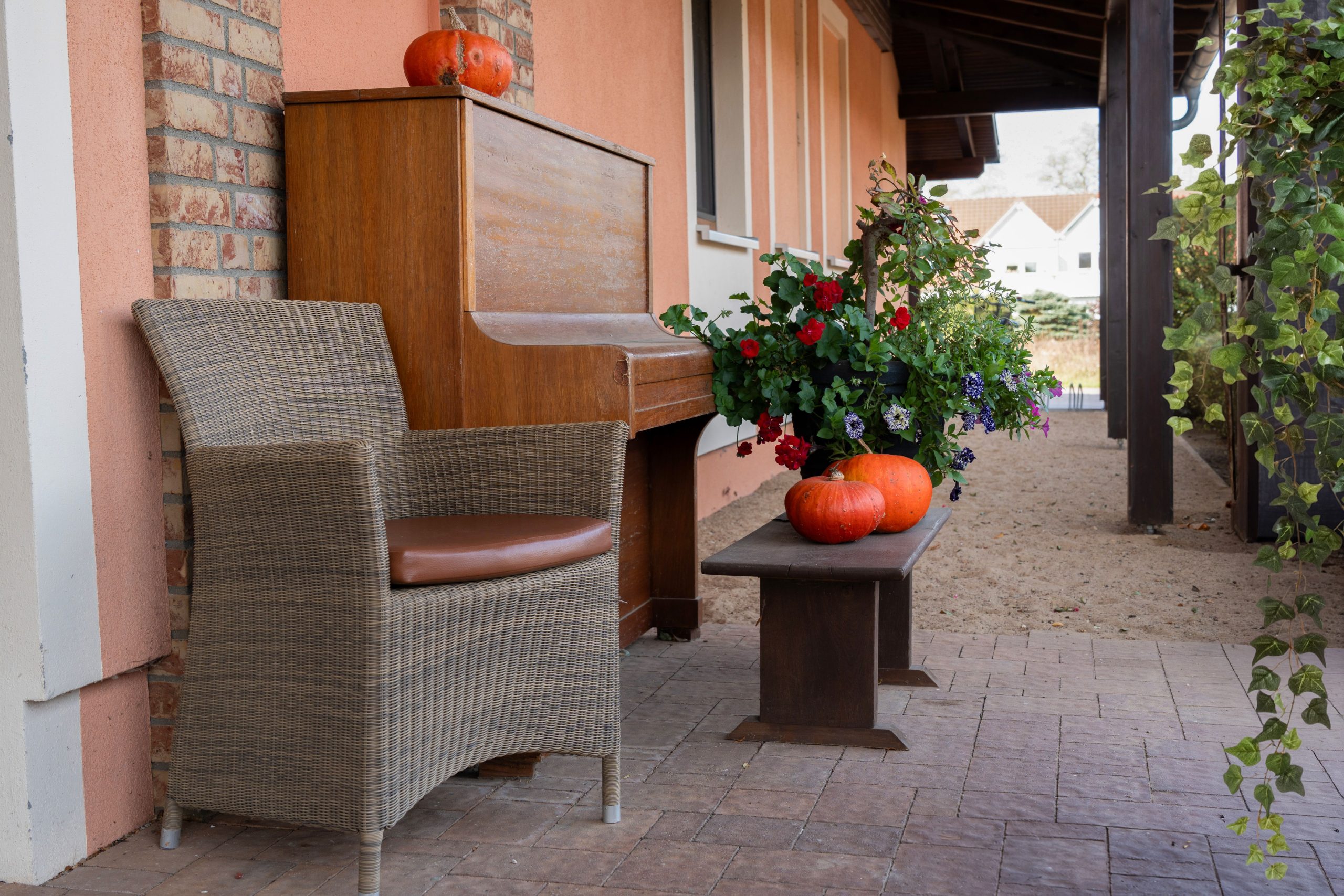 Cozy veranda with a rustic piano, pumpkins, and blooming flowers creating an inviting autumn ambiance.