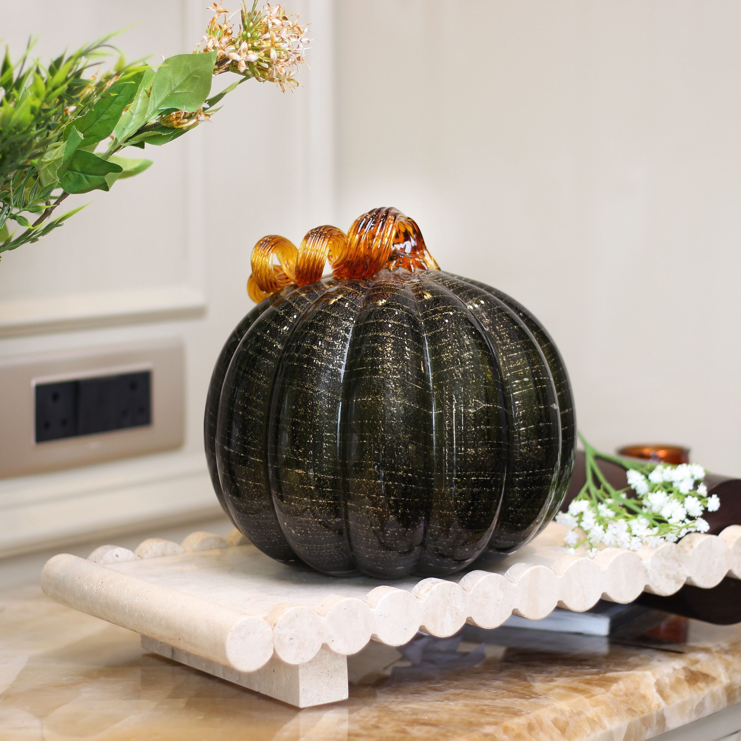 Decorative glass pumpkin on a marble stand, ideal for home decor and autumn-themed arrangements.
