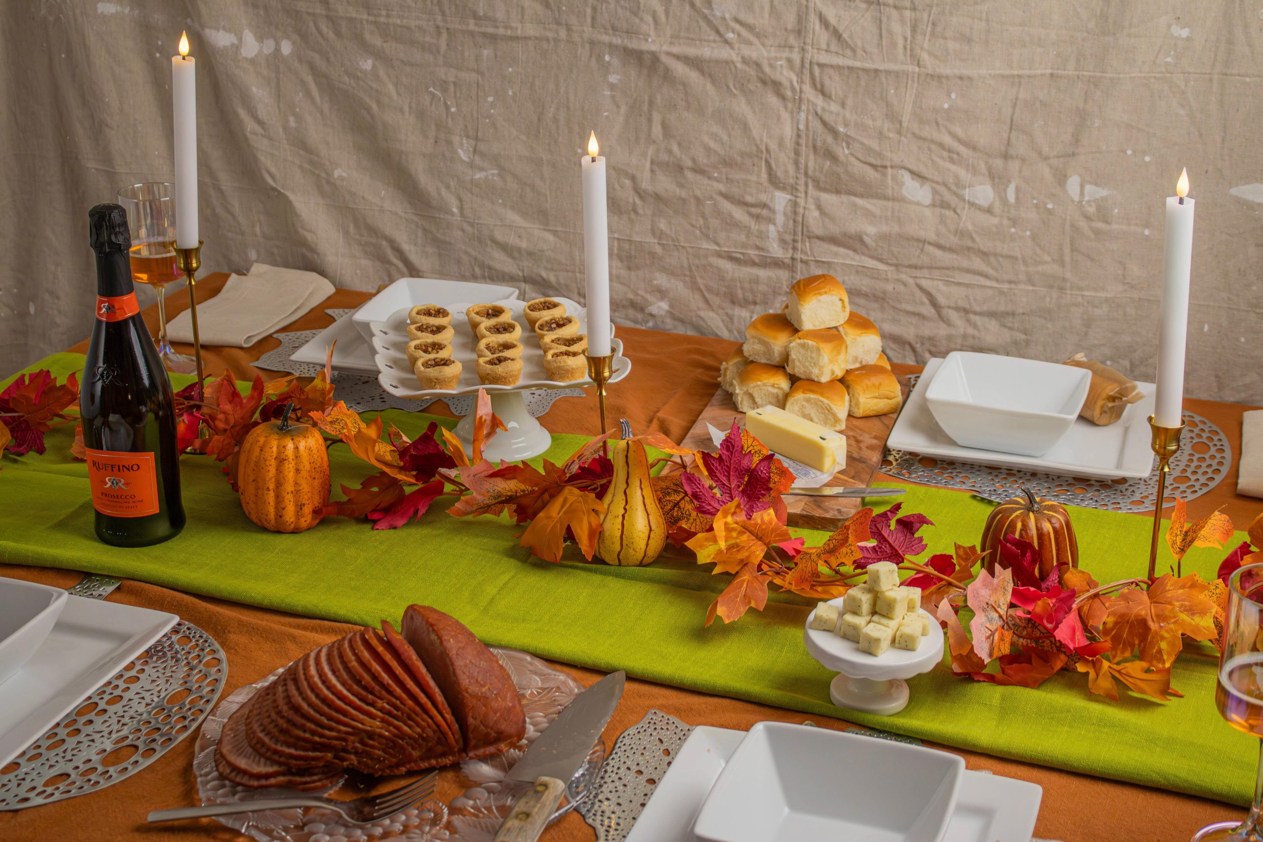 Elegant Thanksgiving table setting with candles, autumn leaves, and festive foods.