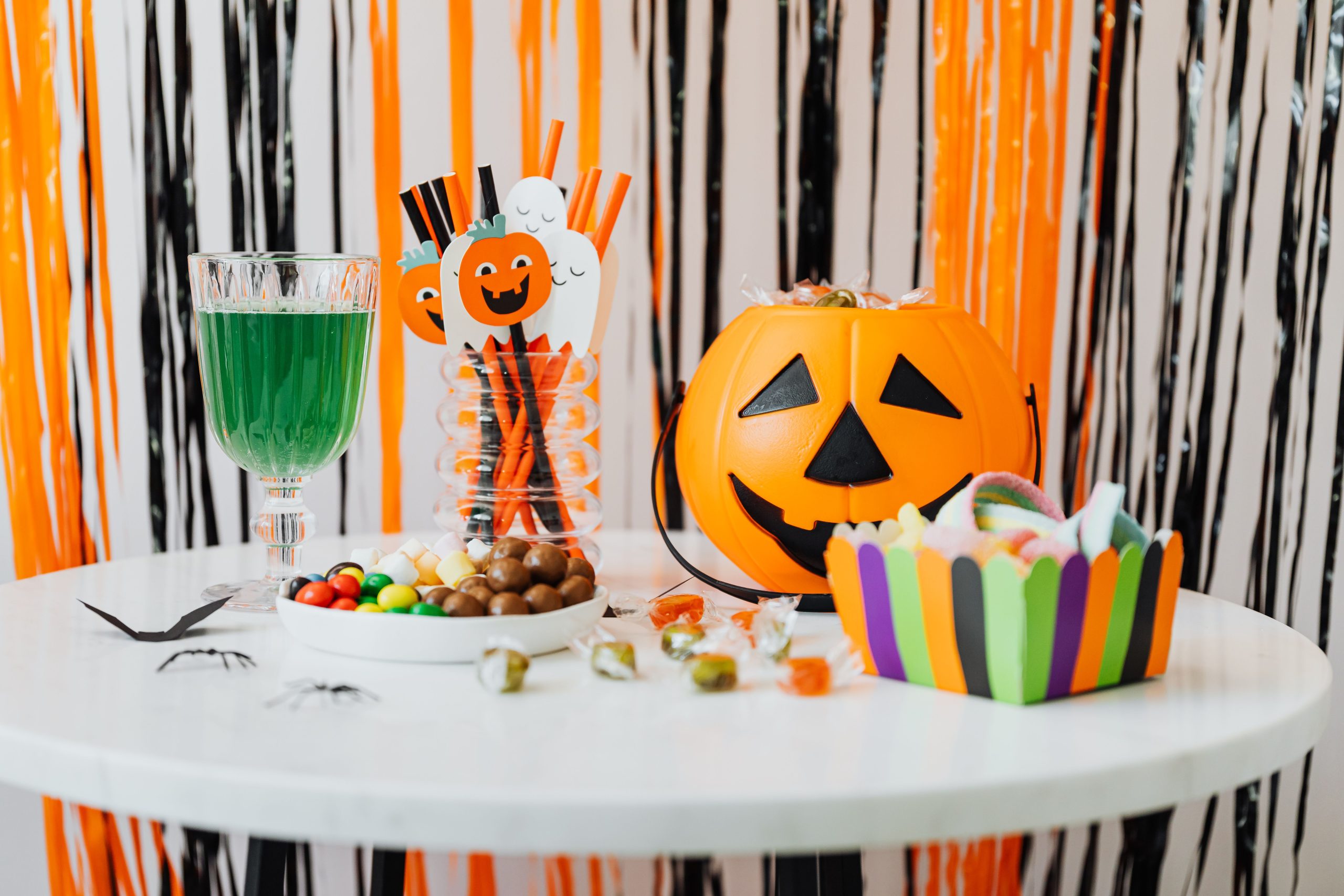 Festive Halloween table with candies, decorations, and a jack-o'-lantern bucket indoors.