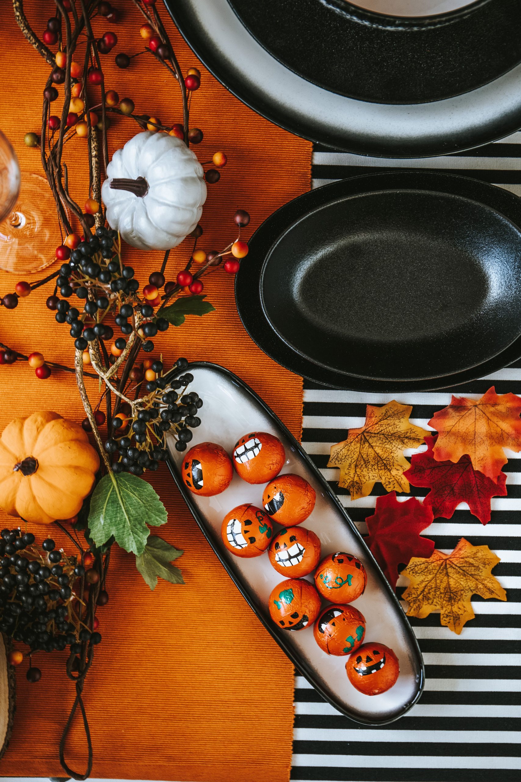 Festive Halloween table with painted pumpkins, berries, and autumn leaves.