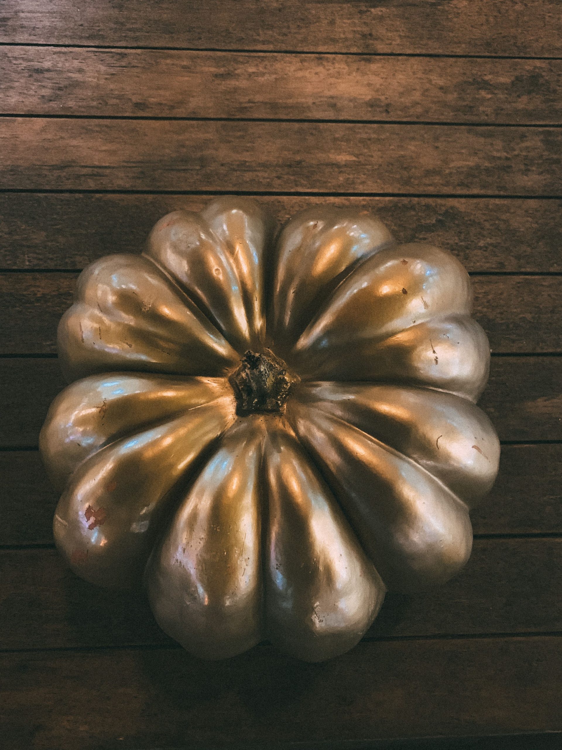 Glossy metallic pumpkin decor on rustic wooden background.