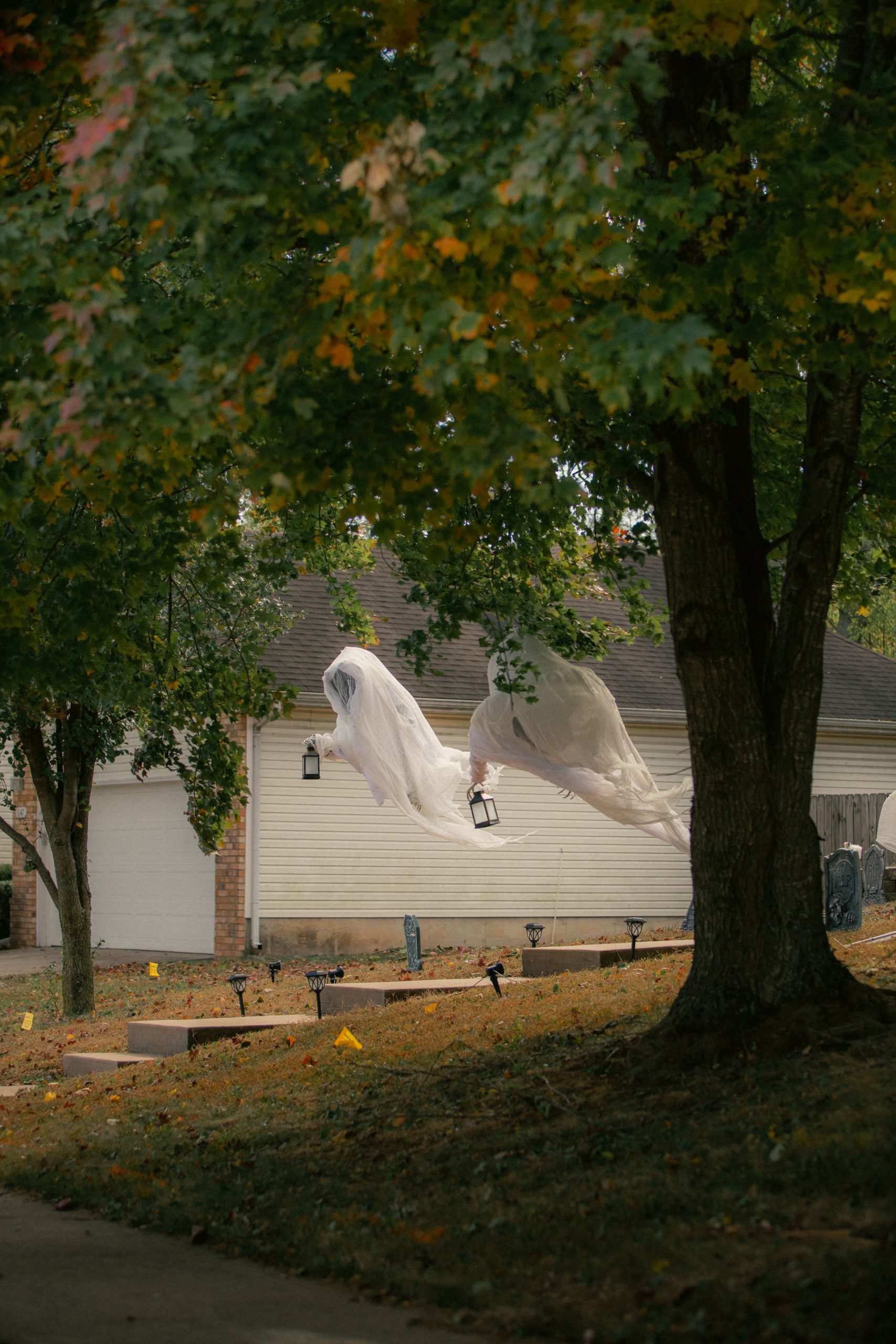Halloween ghost decorations hanging in an autumn yard create a spooky and festive atmosphere.