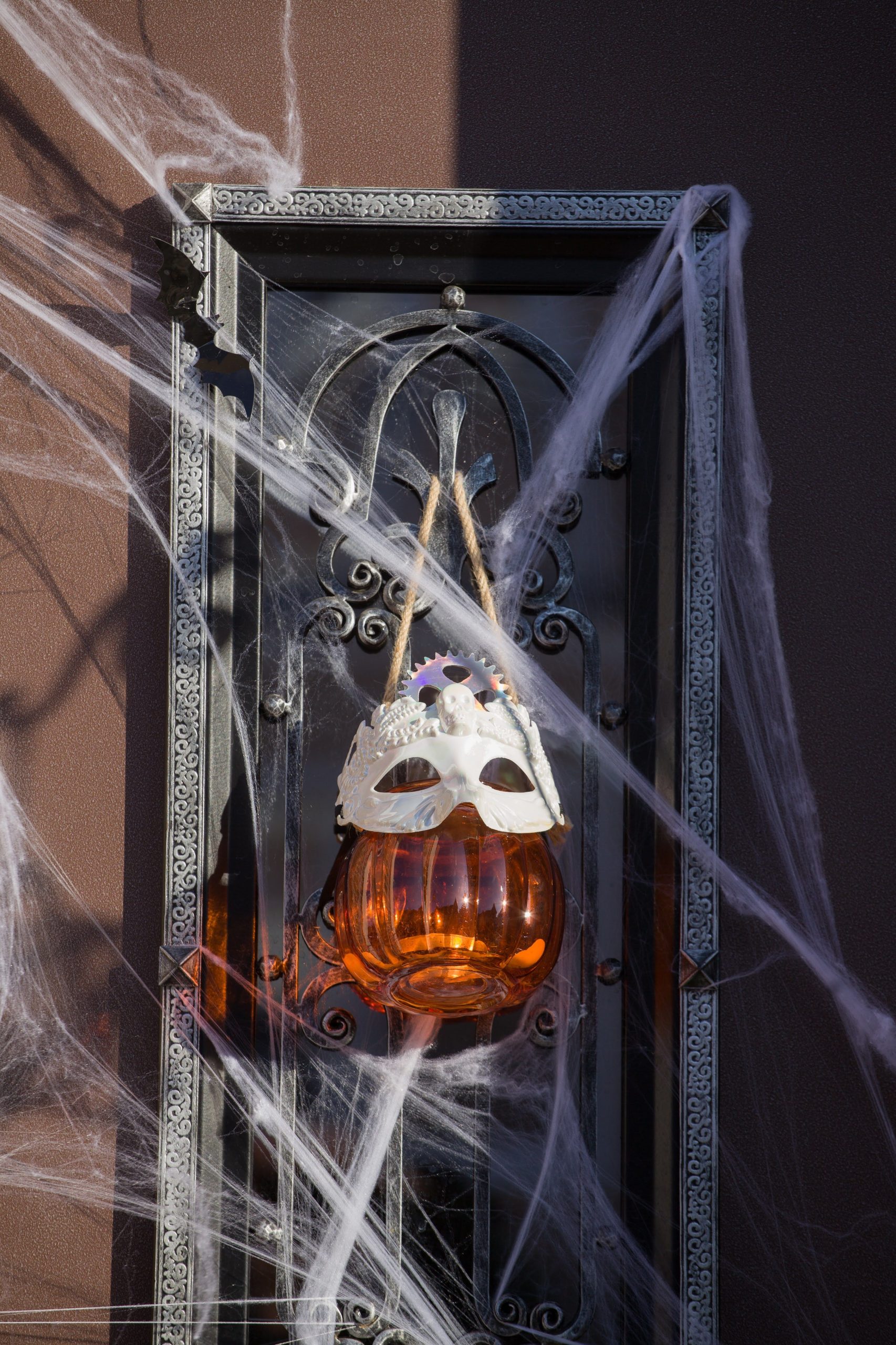 Halloween-themed decor featuring a pumpkin lantern with a mask, surrounded by cobwebs on a wrought iron frame.