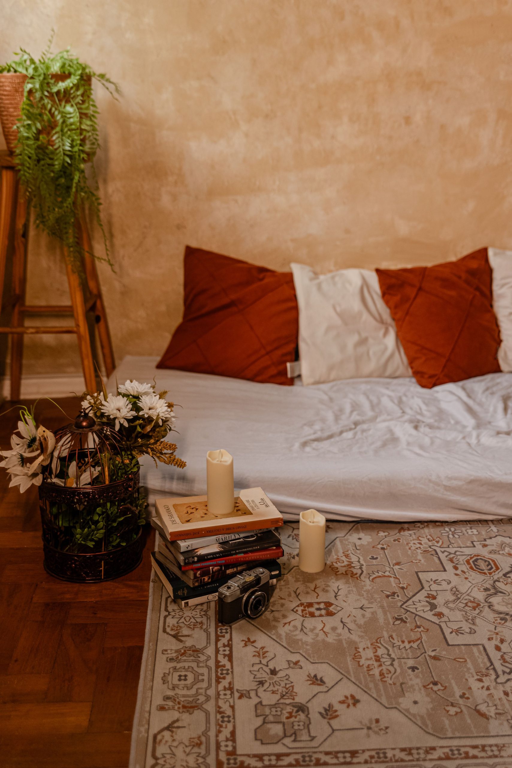 Inviting bohemian bedroom with pillows, books, candles, and plants for a cozy atmosphere.