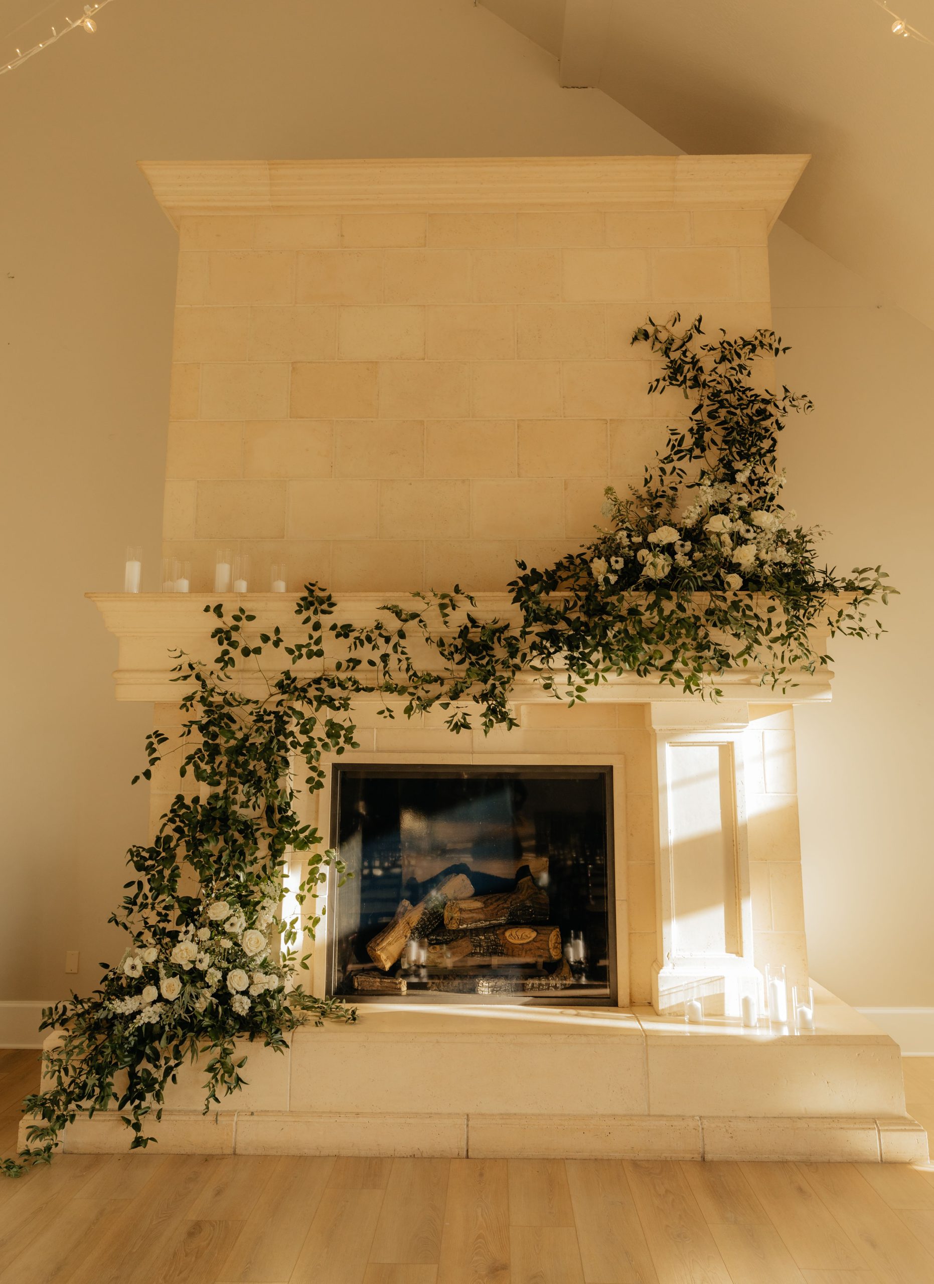 Luxurious stone fireplace adorned with elegant green and white floral garland in a bright interior.
