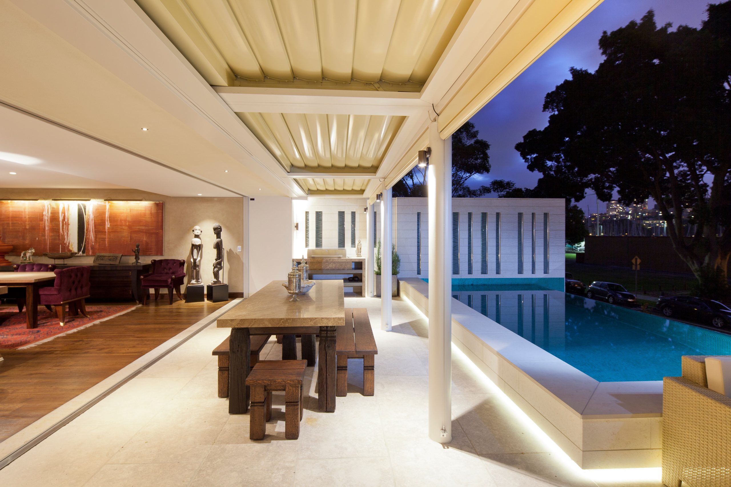 Modern luxury patio with dining set and poolside view at dusk, offering elegance and relaxation.