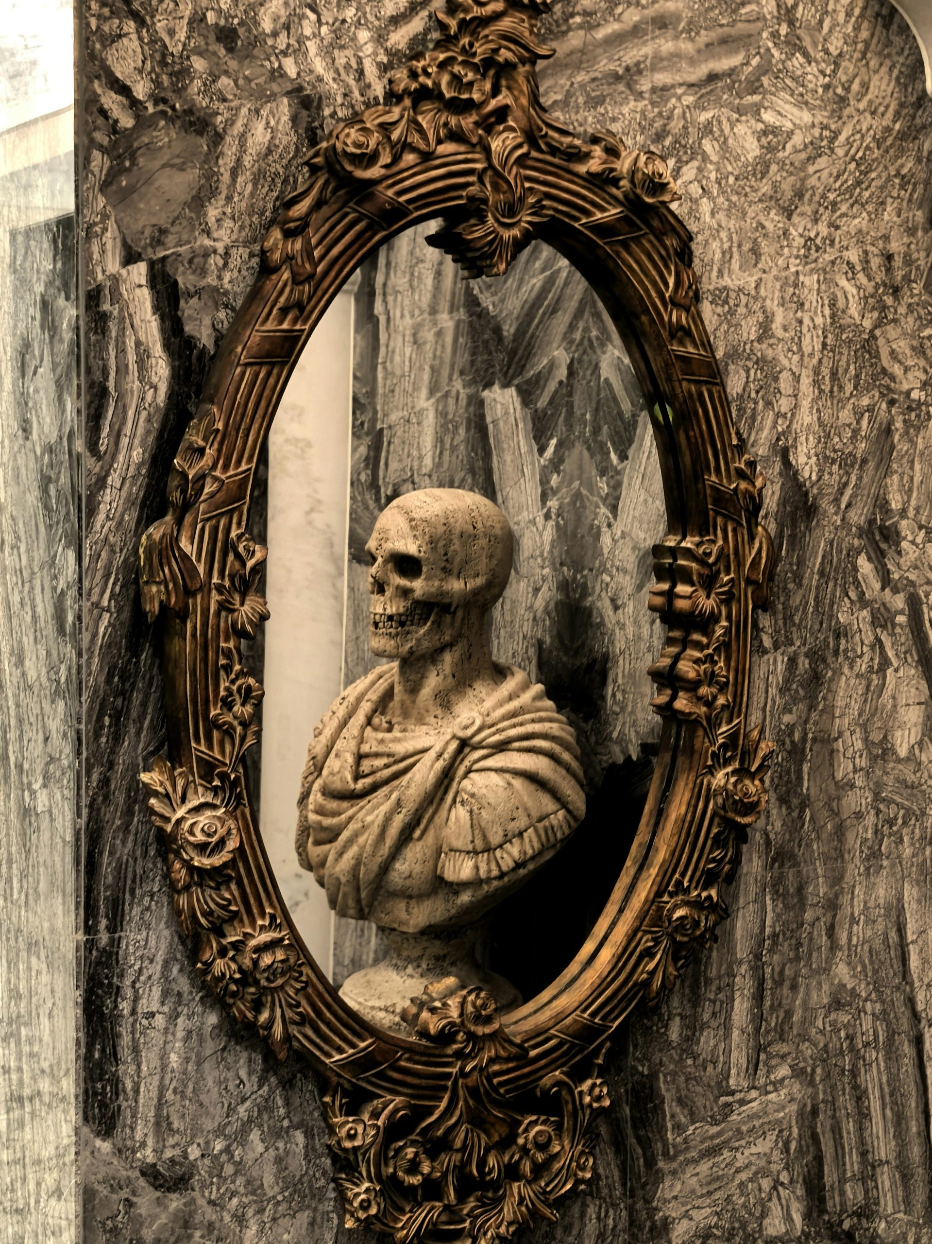 Ornate mirror reflects a marble bust of a skeleton