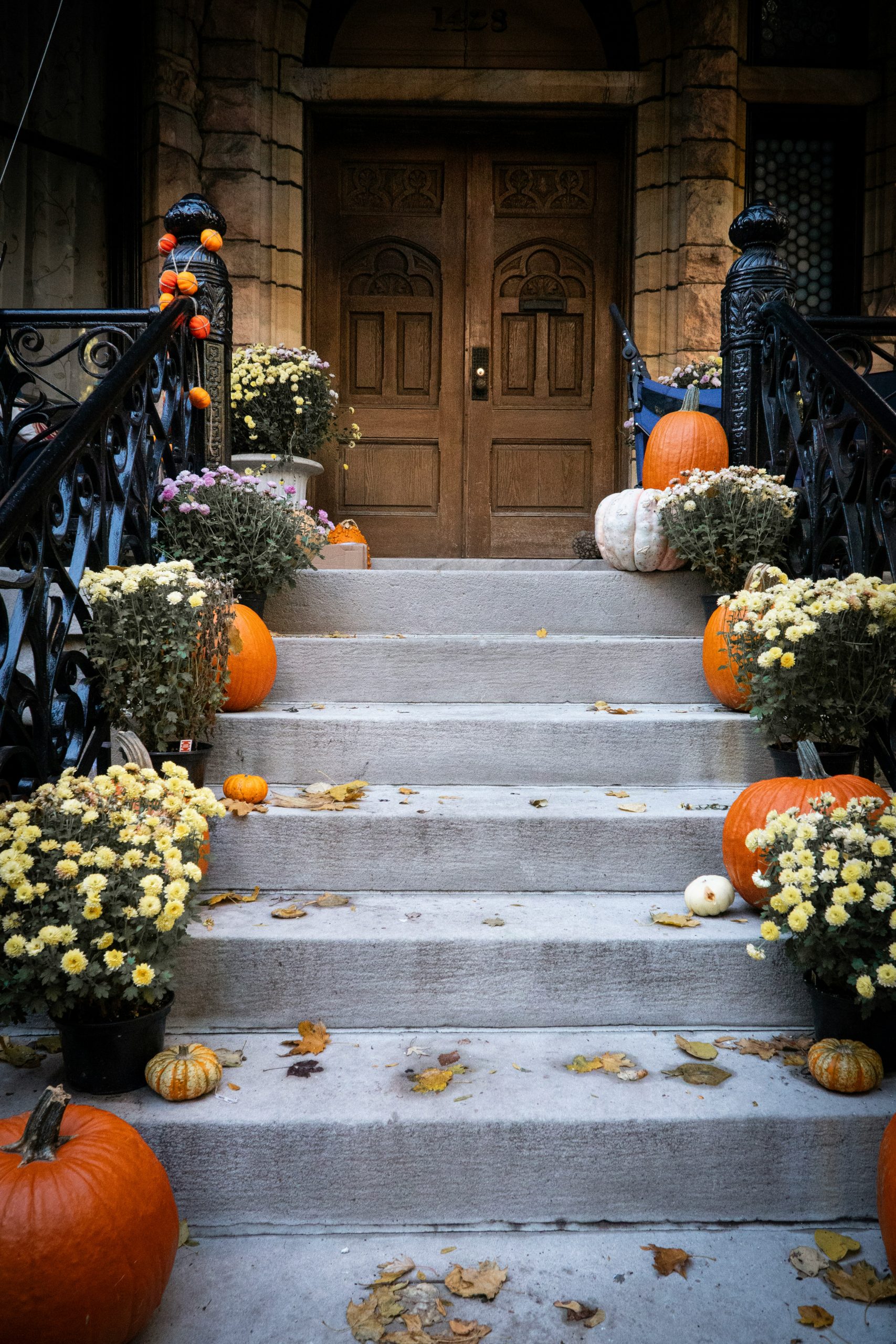 Pumpkins and mums decorate steps of a brownstone.