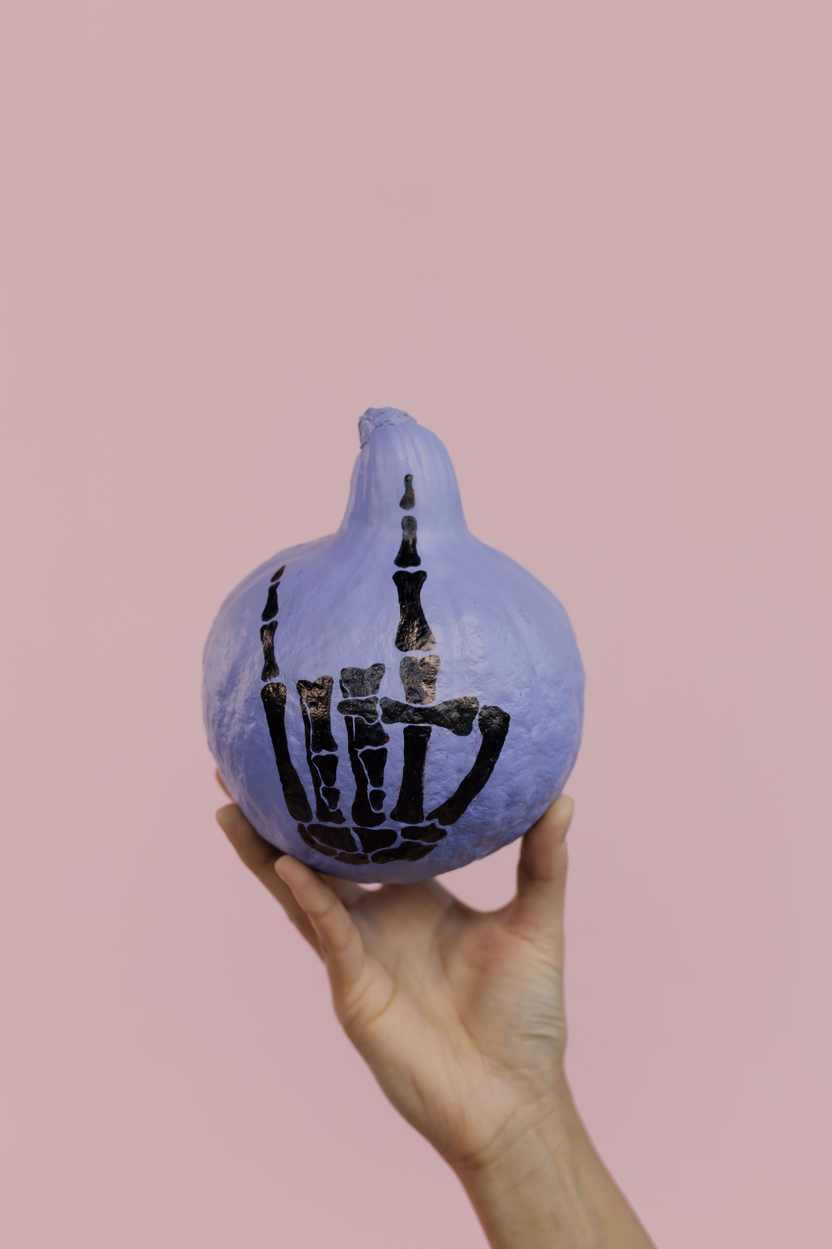 Purple pumpkin with a skeleton design held against a pink background, perfect for Halloween themes.
