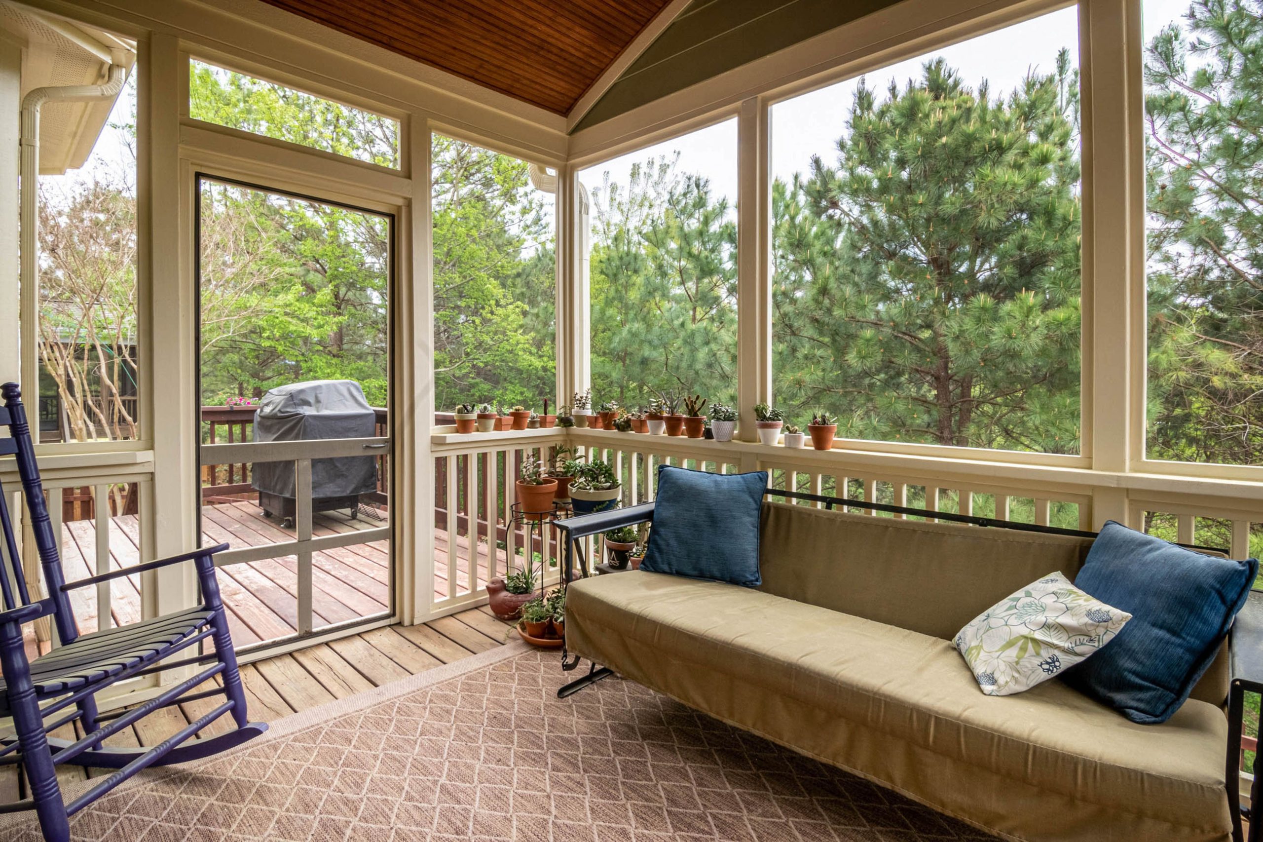 Relaxing screened porch with couch, plants, and outdoor greenery view.