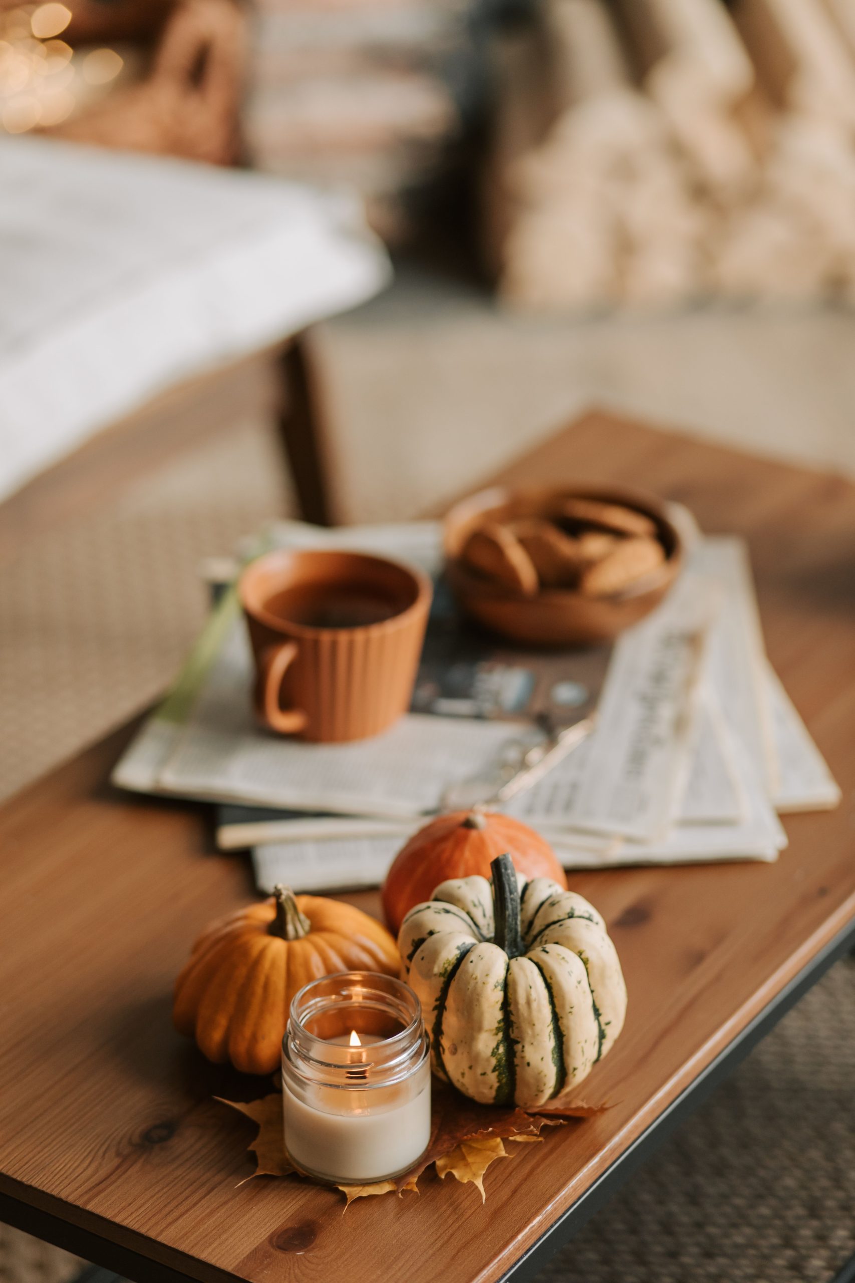 Rustic autumn setup with pumpkins, candle, and coffee inside home.