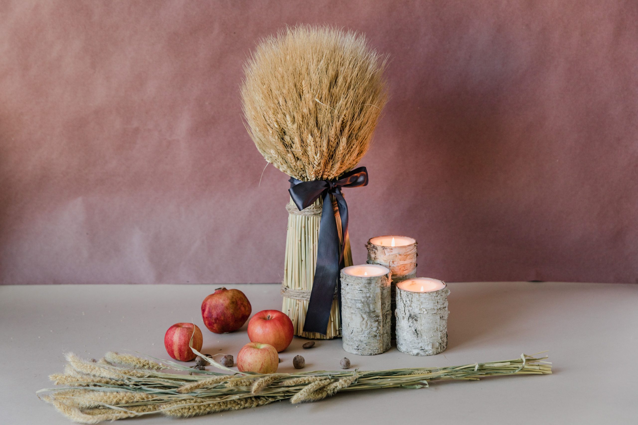 Rustic still life featuring apples, wheat arrangement, and candles on a table.