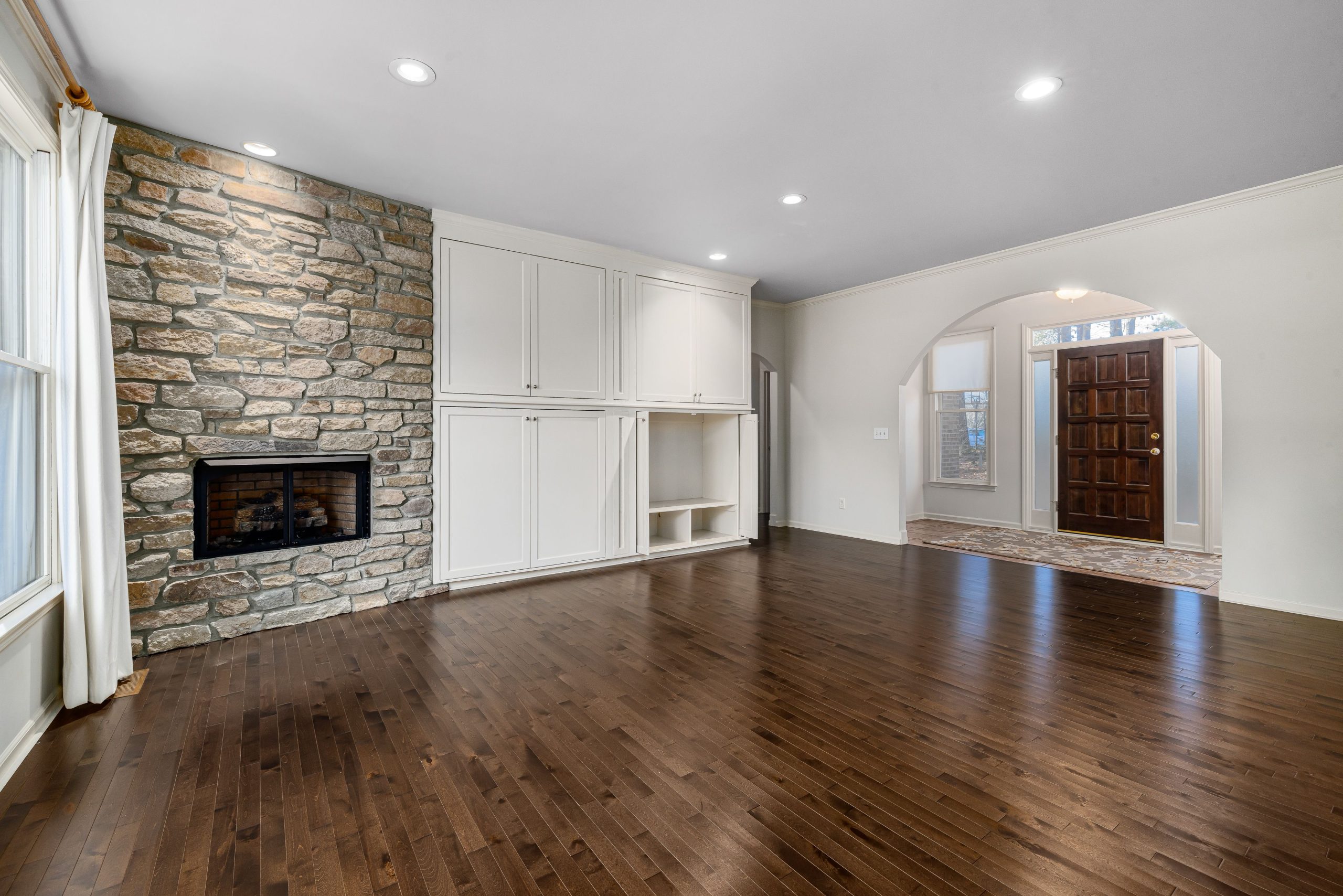 Spacious modern living room with stone fireplace, wooden flooring, and natural light.