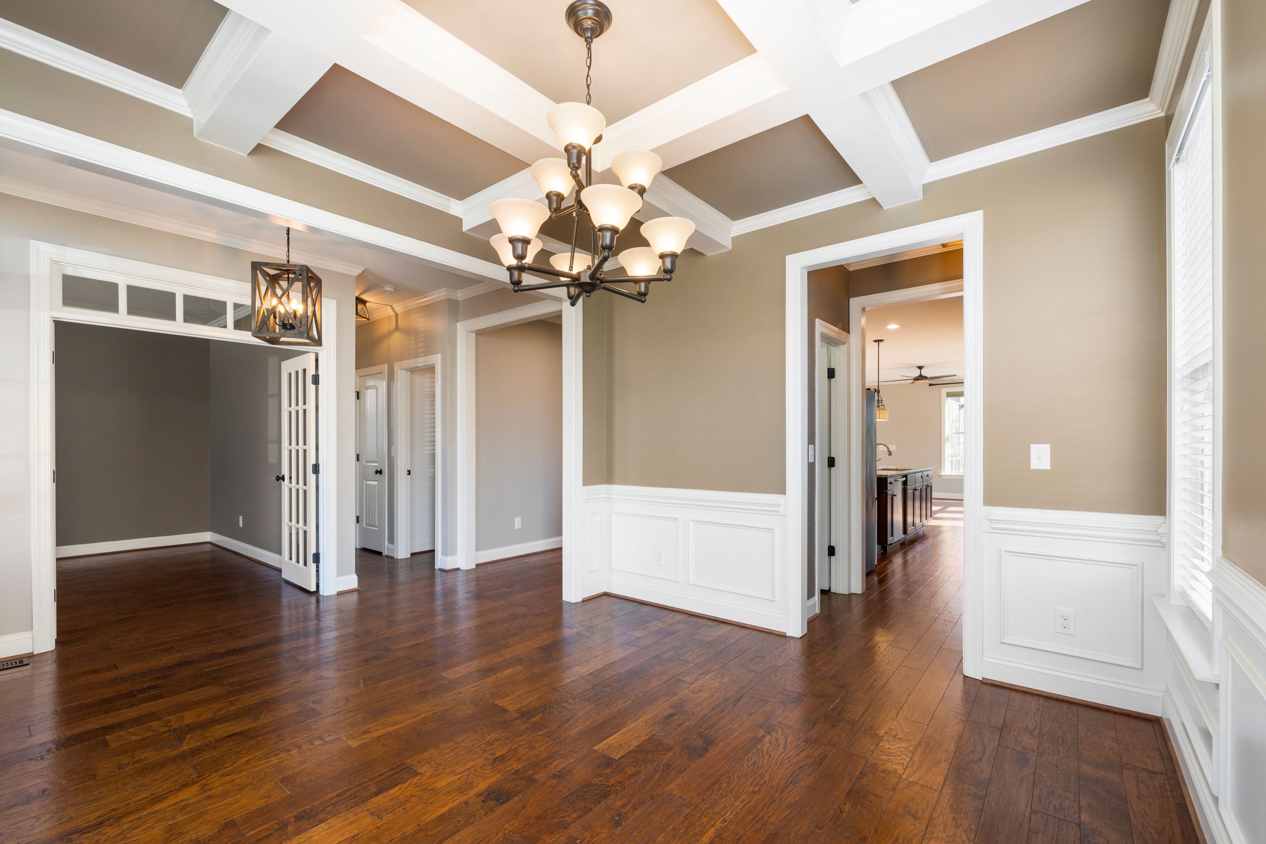 Spacious room showcasing elegant design with hardwood floors, chandelier, and wainscoting.
