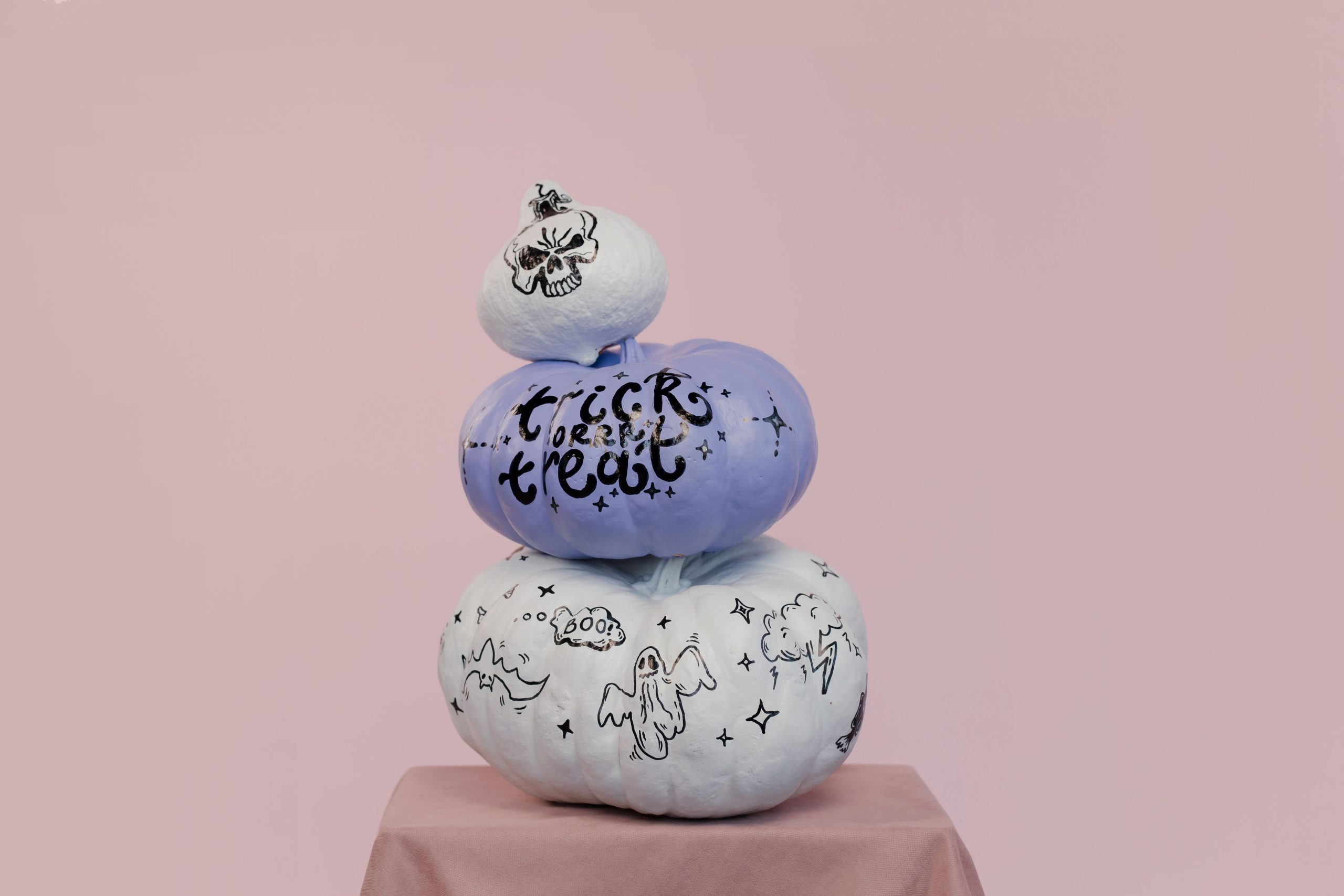 Three stacked Halloween pumpkins with hand-drawn spooky designs on a pastel background.