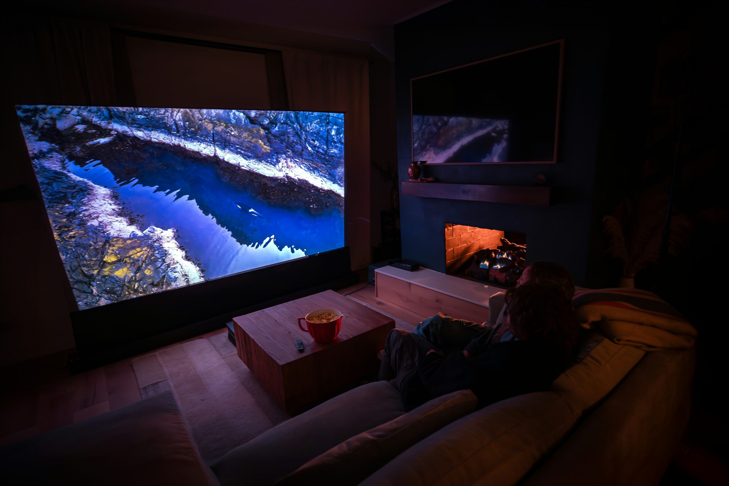 Two people sitting on a couch watching nature river landscape on AWOL Vision 4K UST projector.