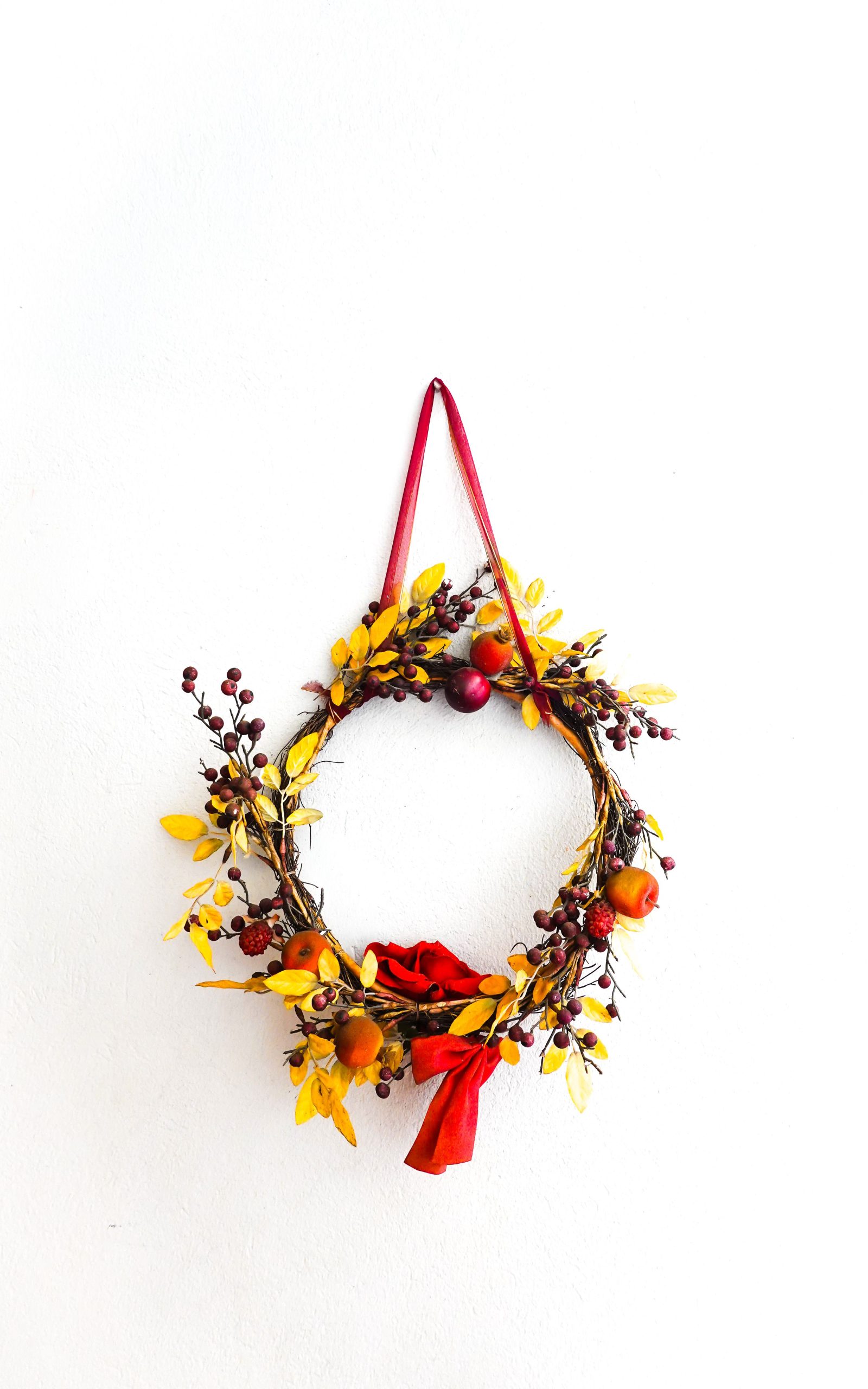 Vibrant autumn wreath with berries and yellow leaves on white wall.