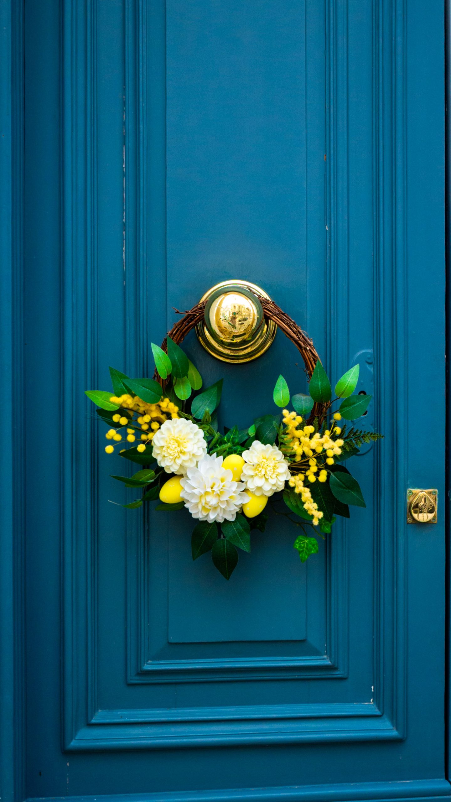 Vibrant floral wreath with yellow and white flowers adorns a stylish blue door for a welcoming touch.