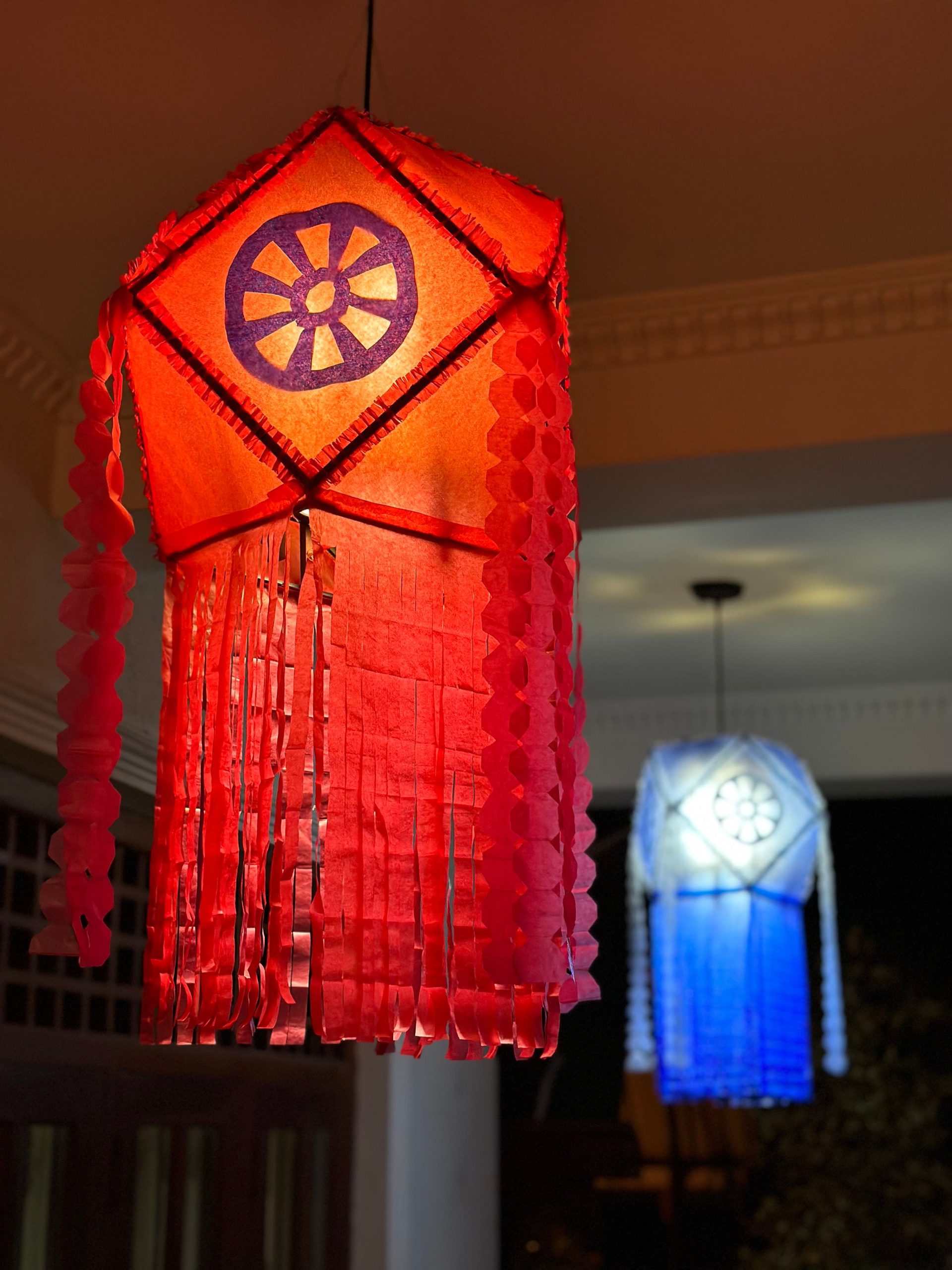 Vibrant red and blue lanterns hanging indoors, illuminating an evening setting.