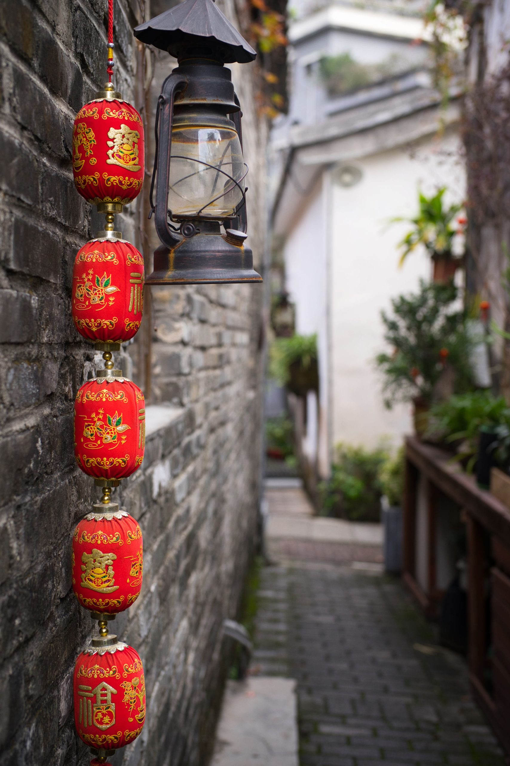 Vibrant red Chinese lanterns hanging next to a vintage lamp in a narrow stone alley.