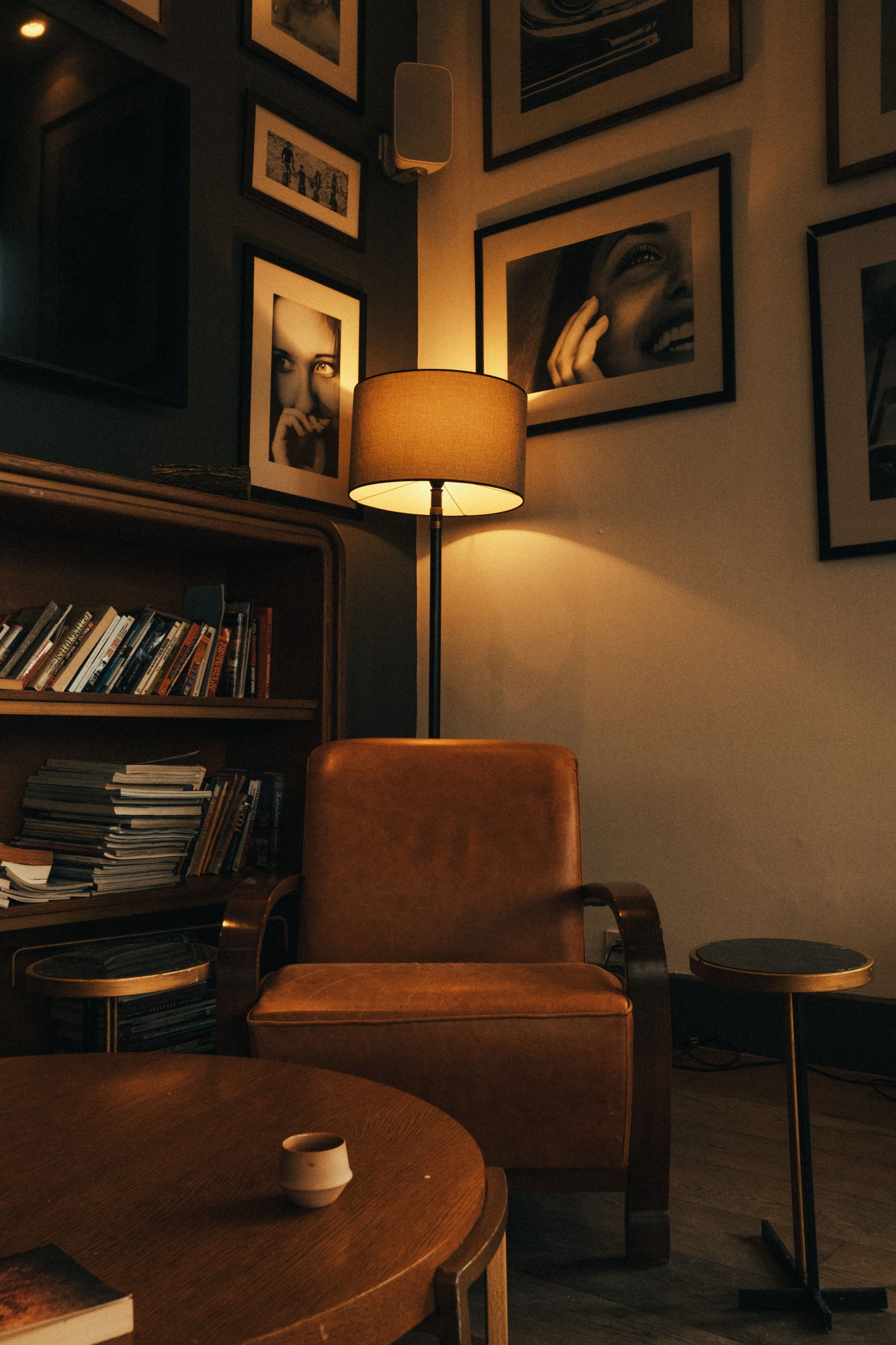 Warm and inviting room with a leather armchair, floor lamp, and art-filled walls.