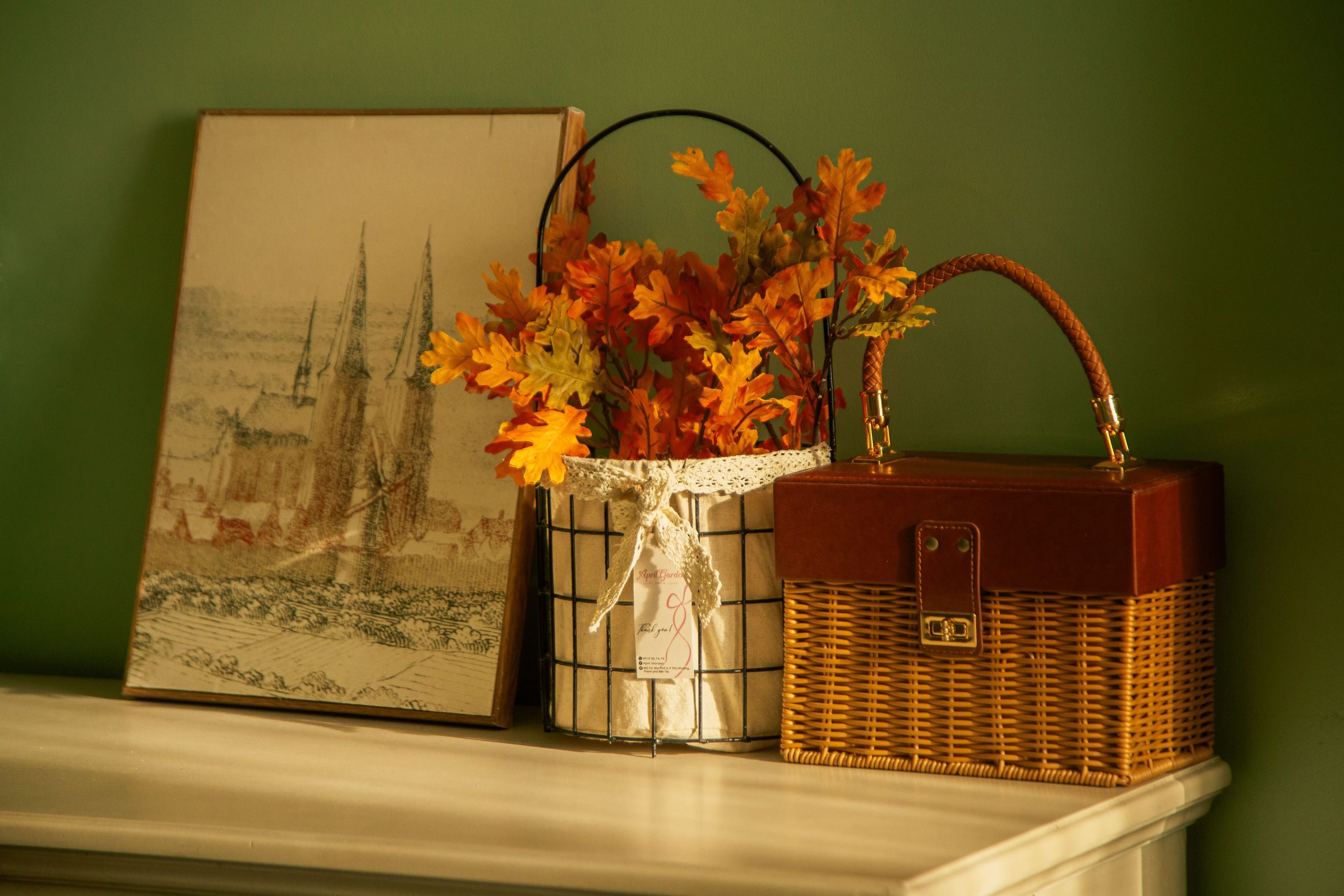 Warm autumn arrangement with flowers, wicker basket, and artwork on a table.