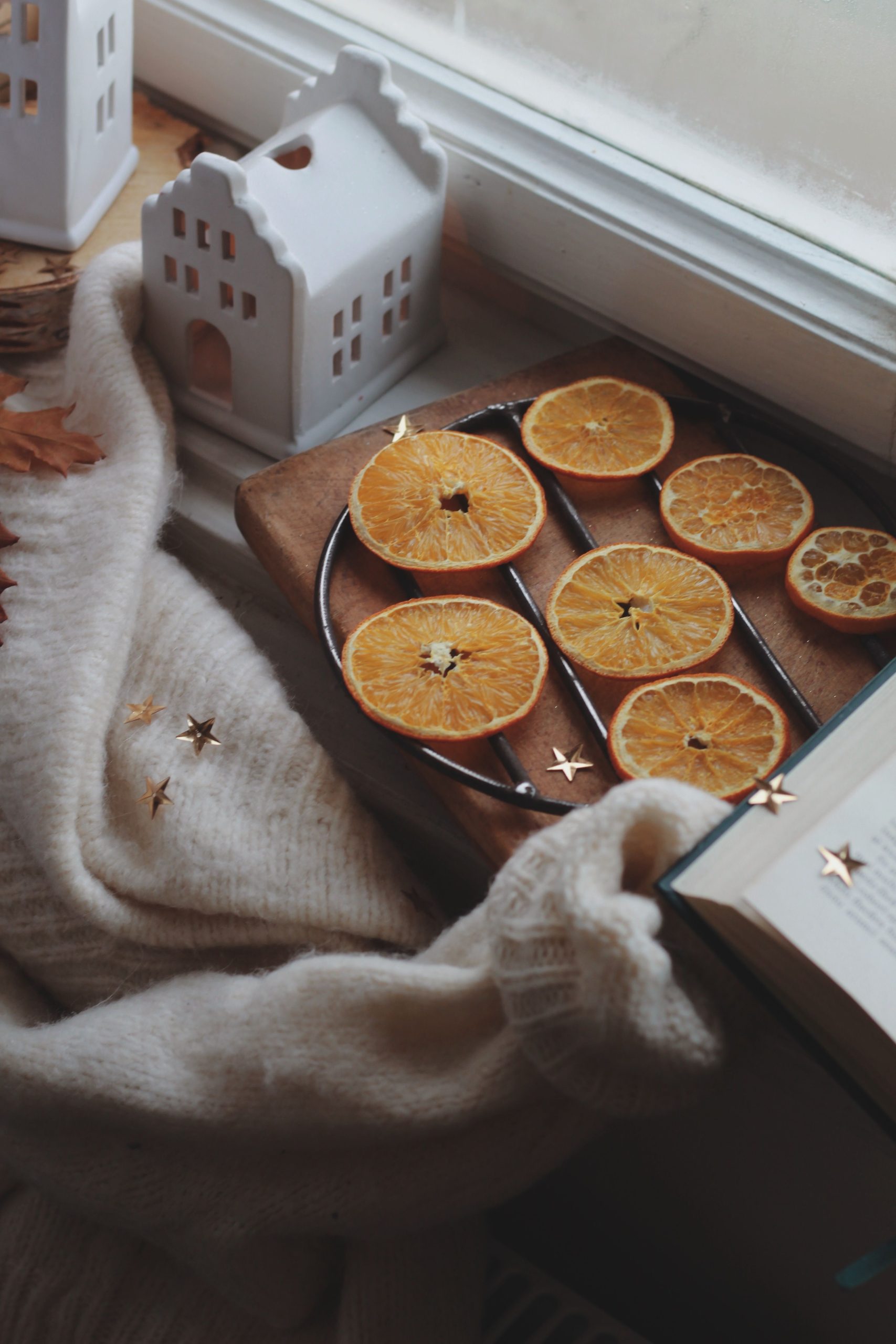 Warm autumn scene with dried orange slices, cozy sweater, and decorative houses by a window.