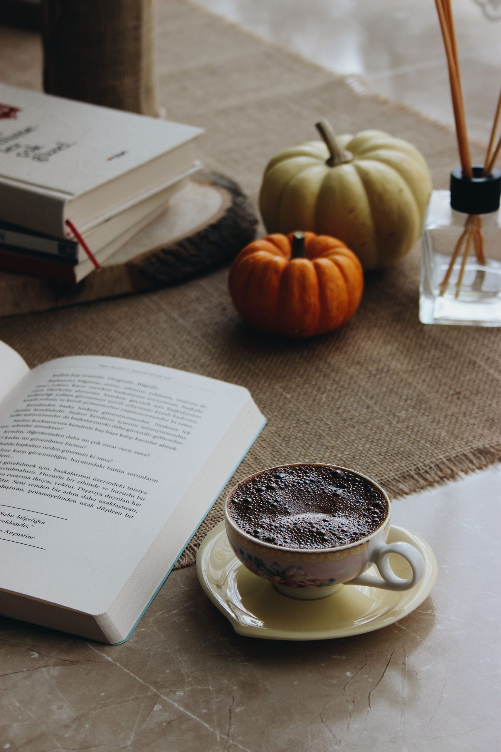 Warm autumn setting with coffee, books, pumpkins, and aromatics. Perfect for fall relaxation.