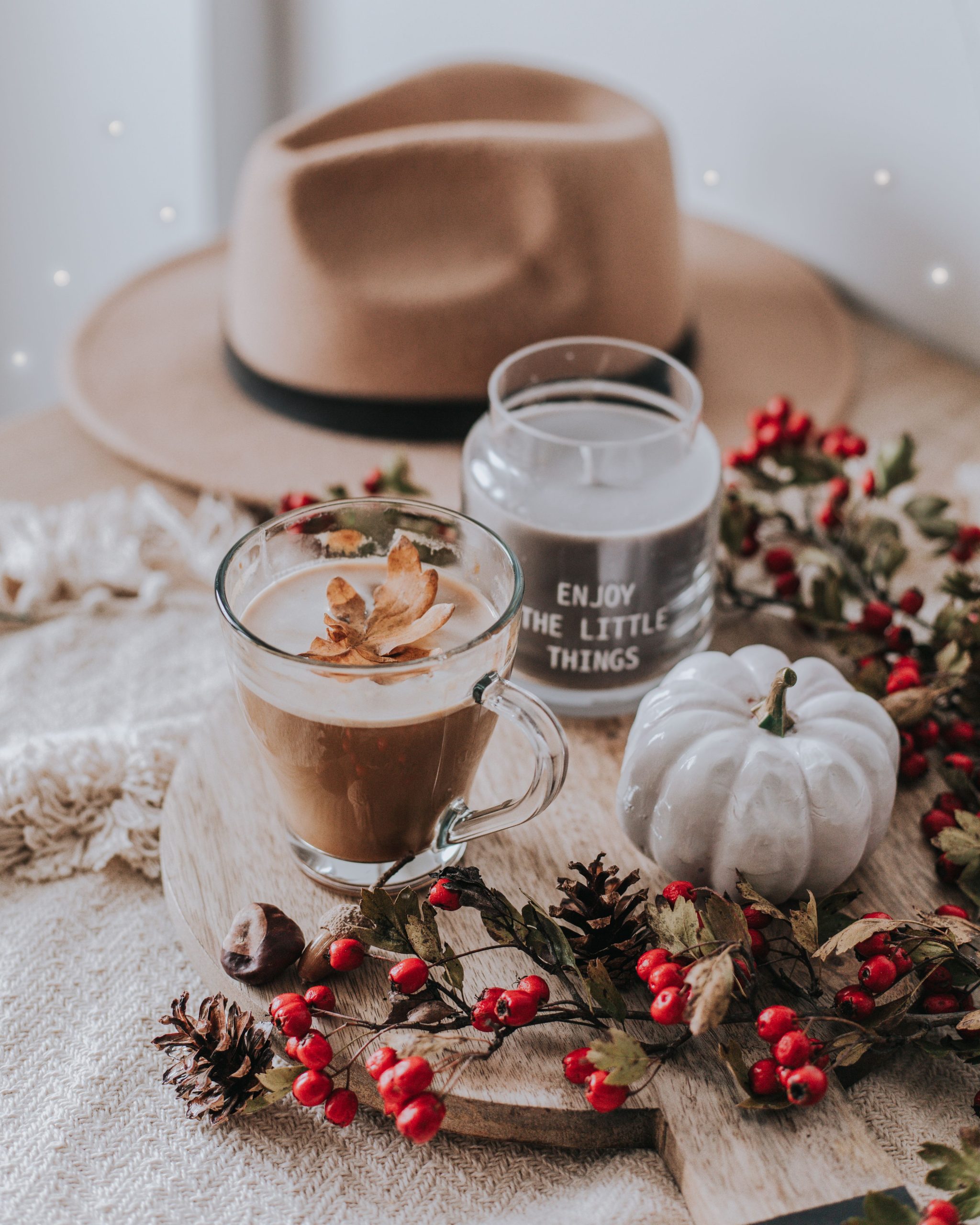 Warm autumn setup featuring coffee, a candle, hat, berries, and decor.
