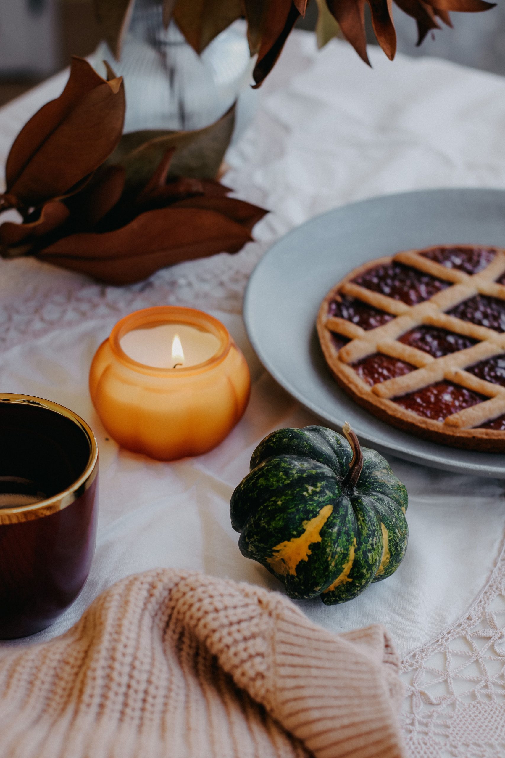 Warm autumn table setting with pie, candle, pumpkin, and cozy sweater, perfect for fall vibes.