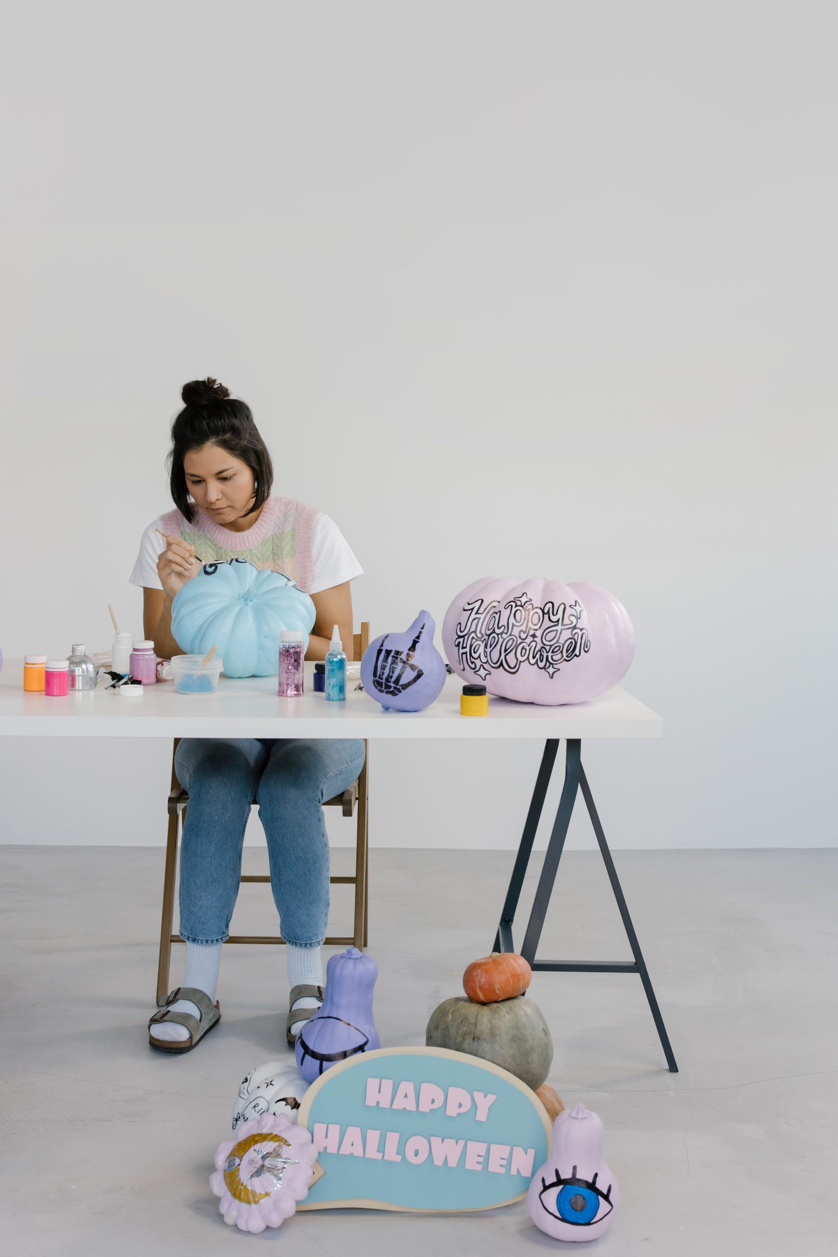 Woman painting pumpkins with Halloween decorations indoors.