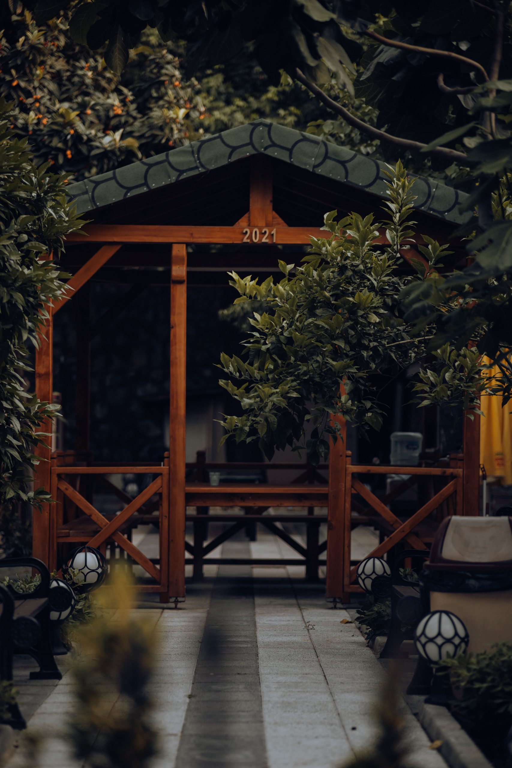 A beautifully crafted wooden gazebo surrounded by lush greenery and decorative lighting.
