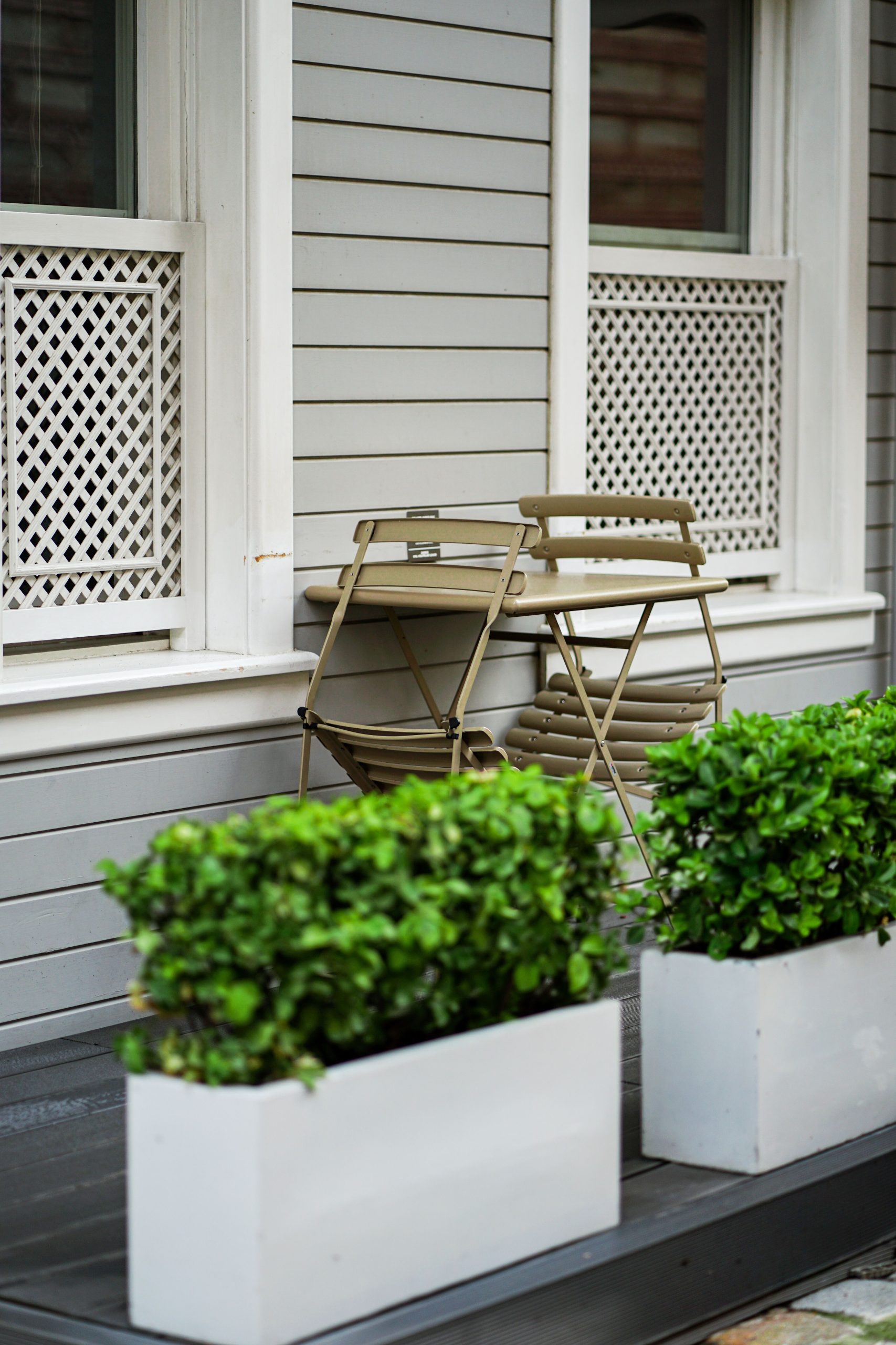 A contemporary patio featuring stacked foldable chairs and lush greenery in planters against a stylish house exterior.