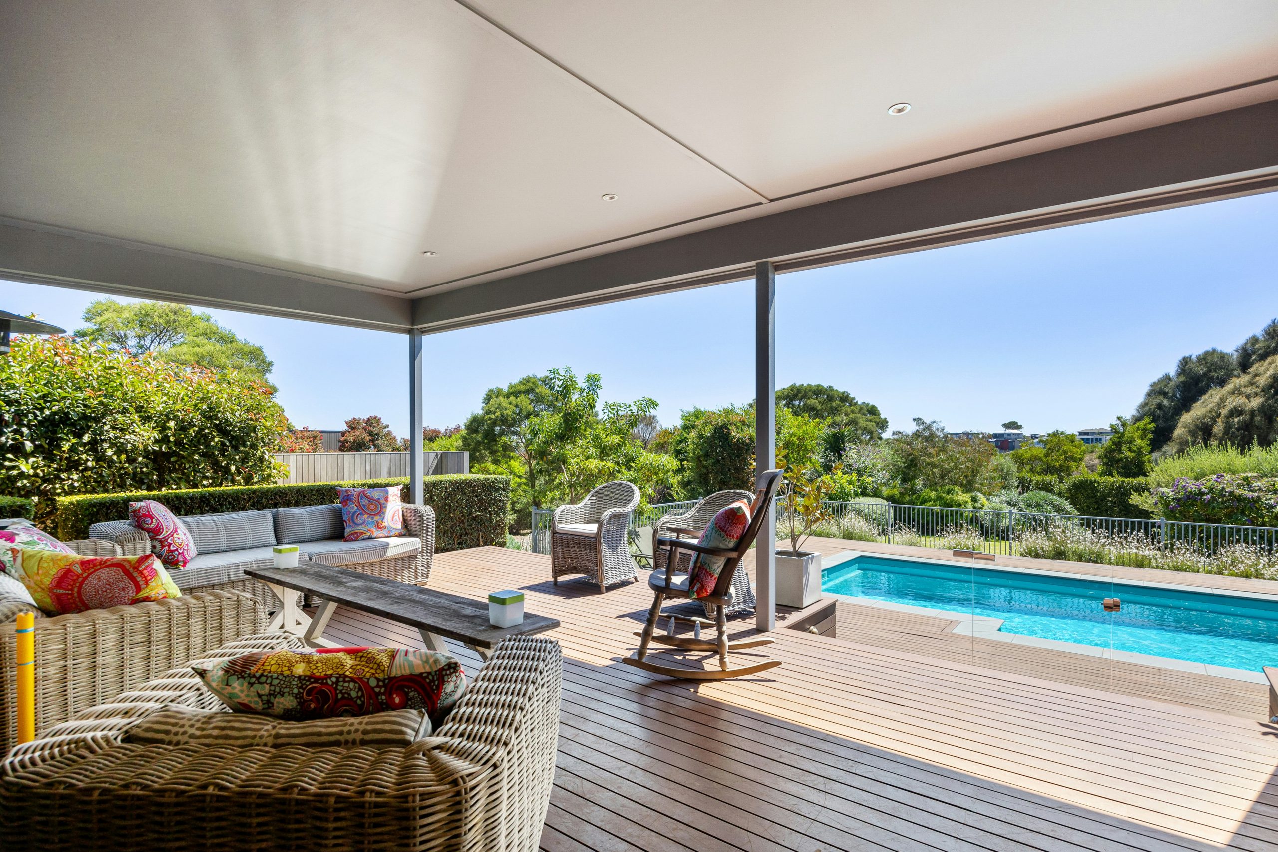 A covered deck with a couch and a table with a bowl of fruit on it