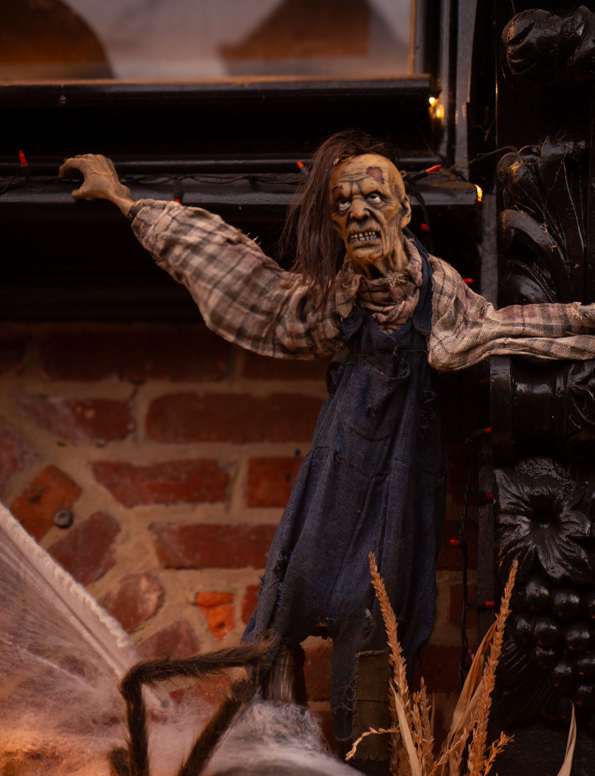 A creepy puppet dressed in plaid and denim overalls on a brick wall, perfect for Halloween decor.