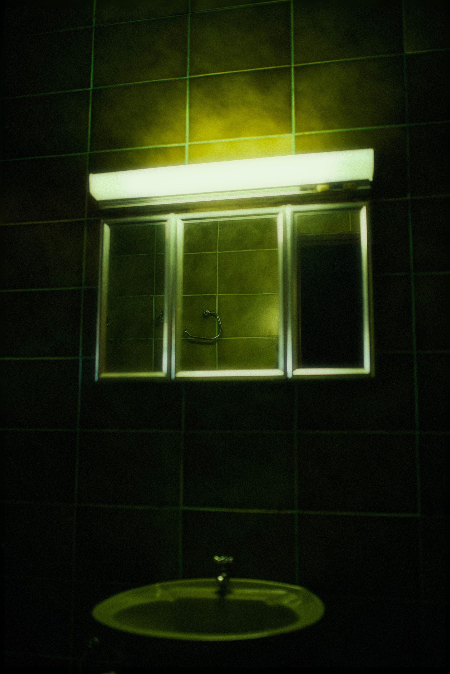 A dimly lit bathroom with green light reflecting off the mirror creating a horror ambiance.