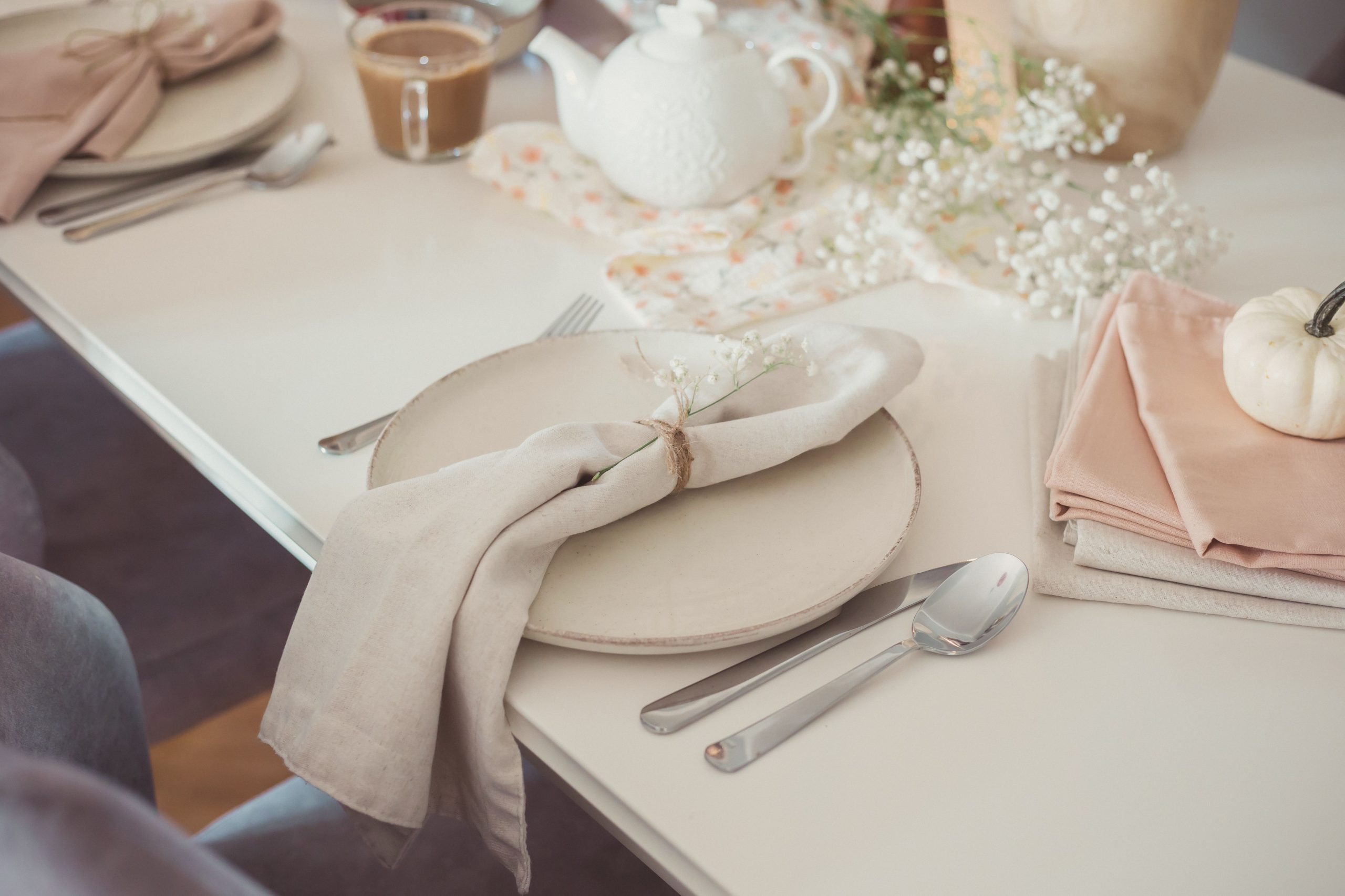 A minimalist autumn table setup featuring a white pumpkin, delicate florals, and elegant tableware.