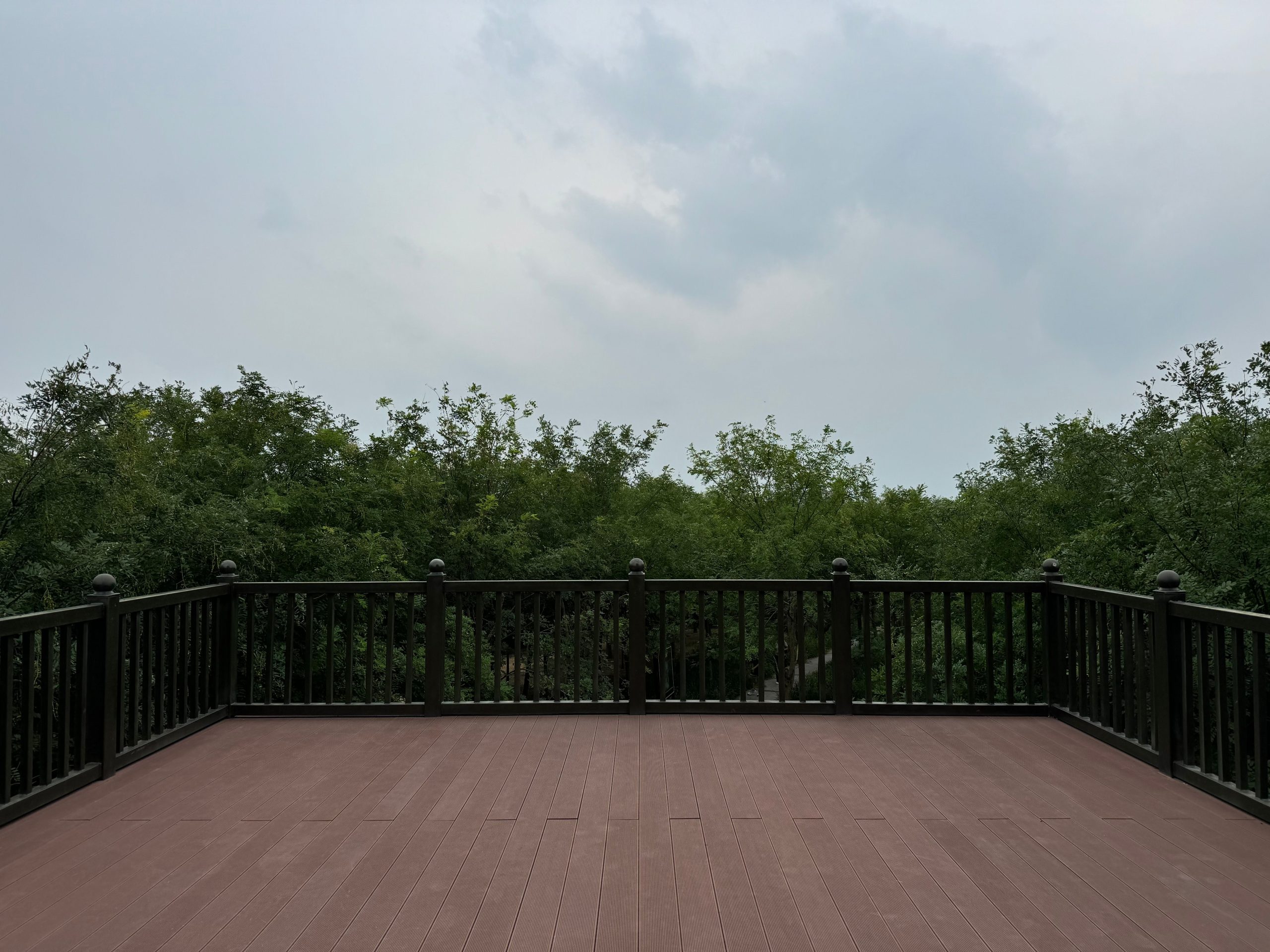 A peaceful wooden deck with a view of lush greenery under an overcast sky. Perfect for outdoor relaxation.