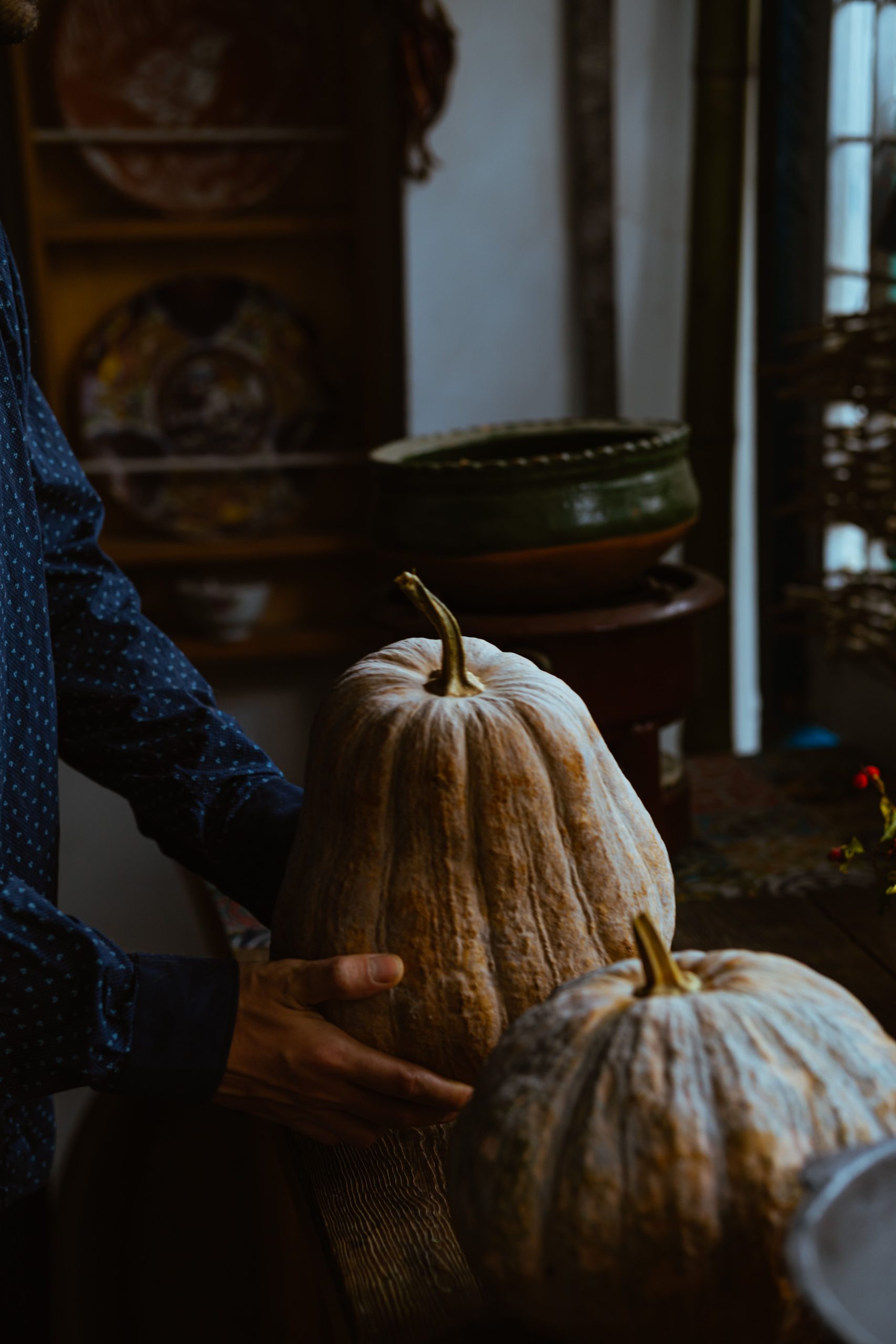 A person holding large gourds in a cozy autumn setting with rustic decor.