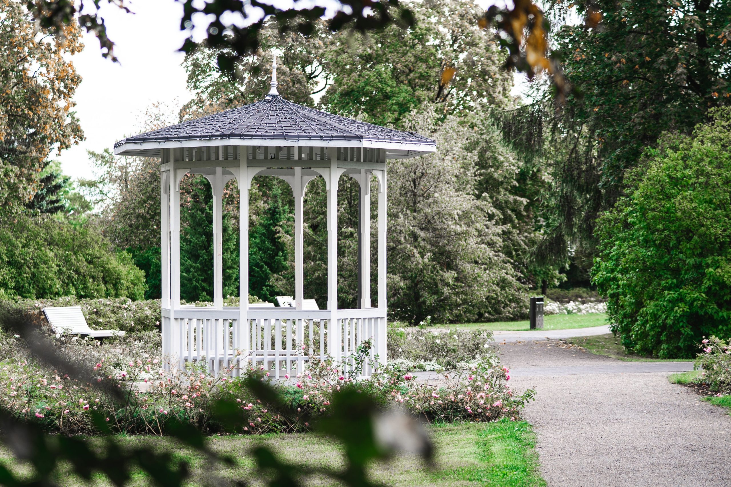 A picturesque white gazebo in a lush green park with surrounding flowers in Keila, Estonia, captured in summer.