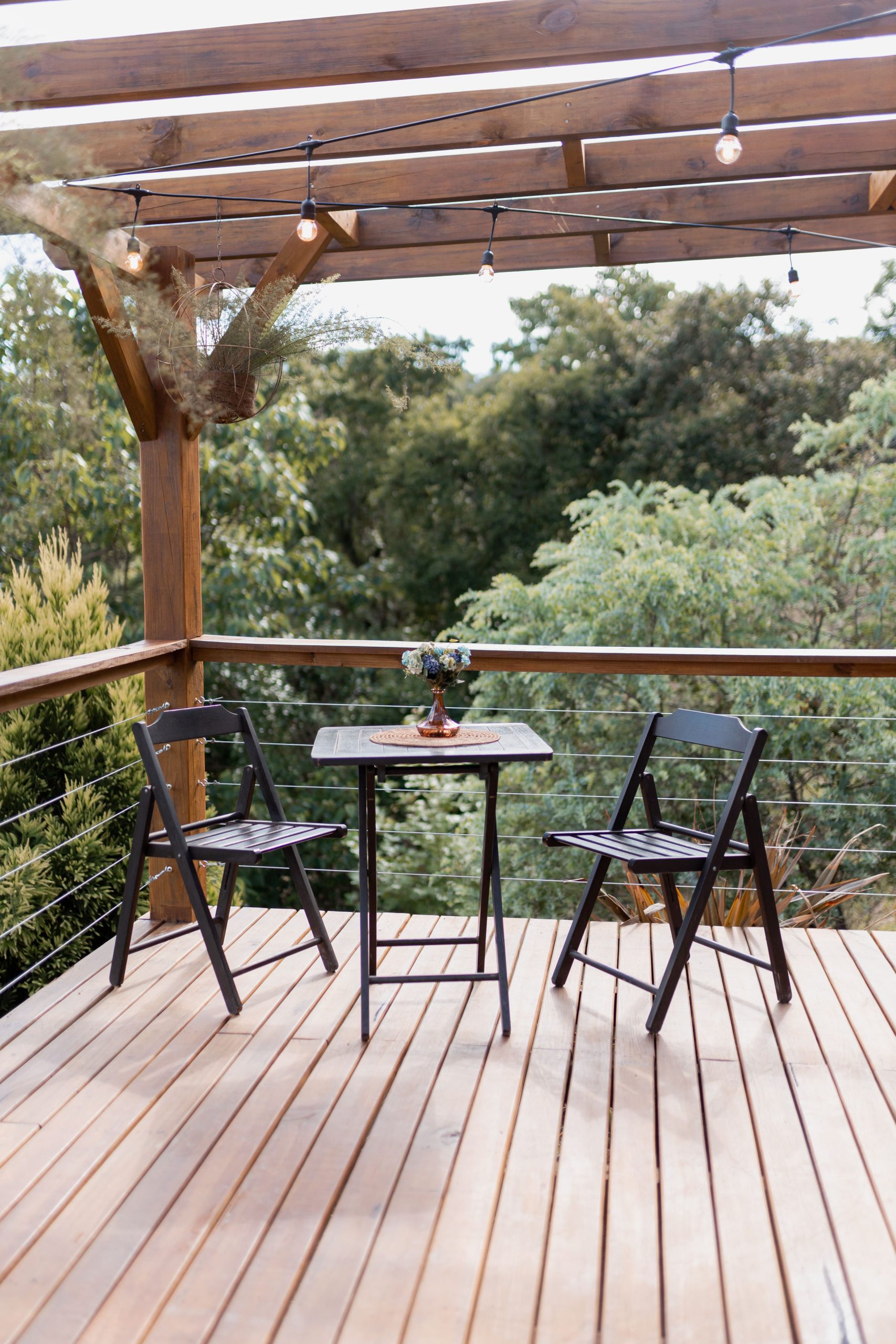 A serene wooden patio with two black chairs and a small table under pergola lights.