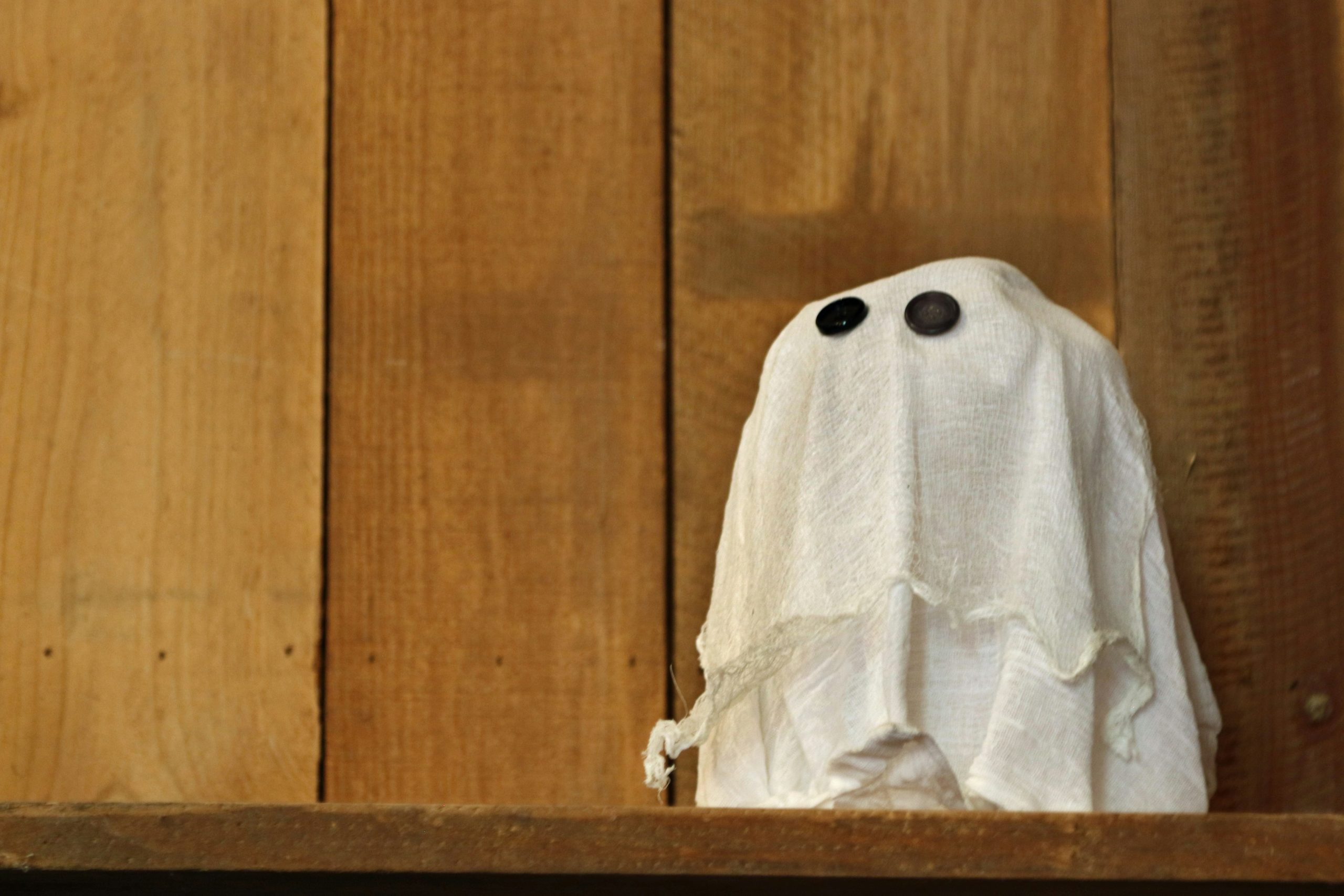 A small ghost decoration with button eyes on wood