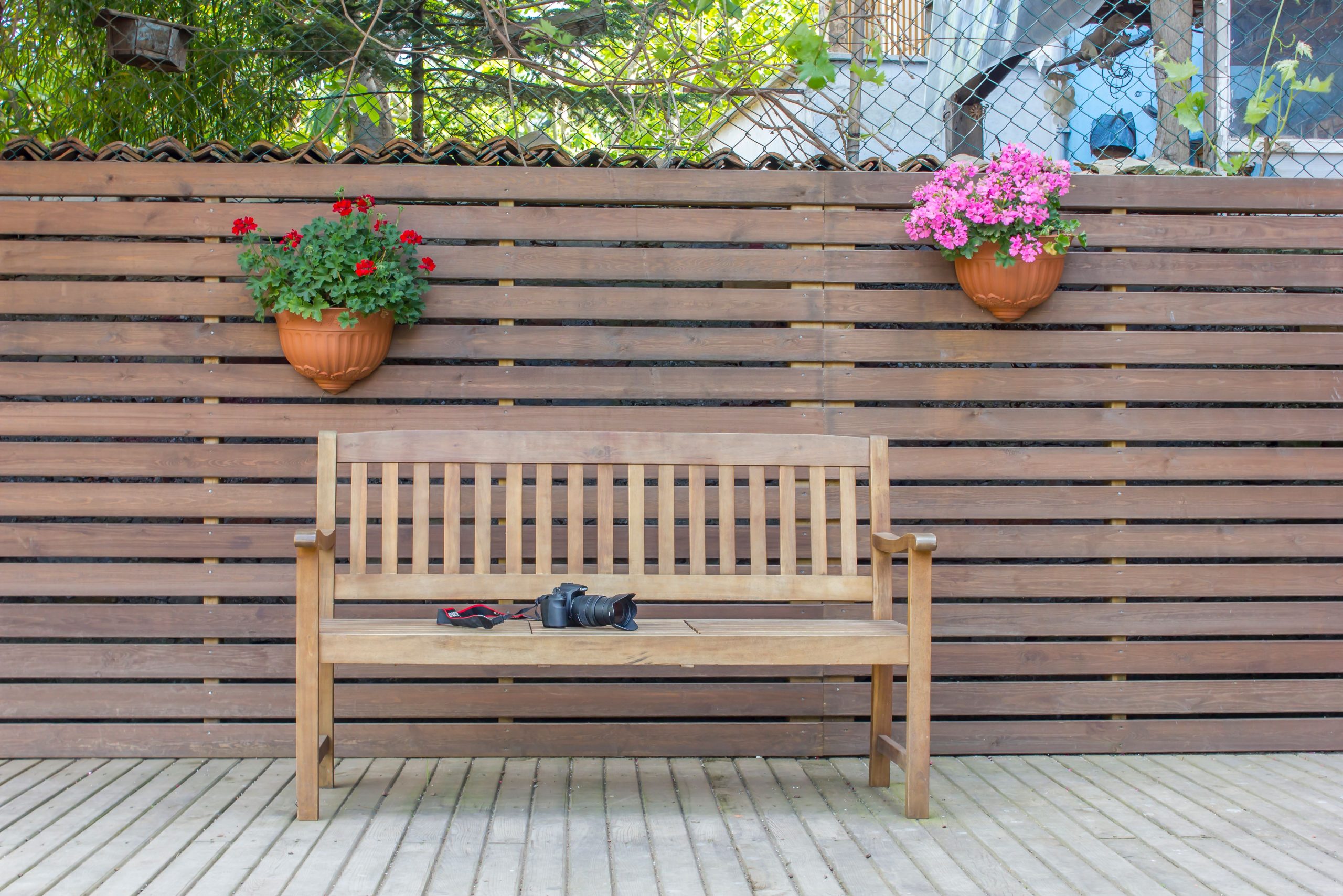 A wooden bench with potted flowers against a wooden fence in a peaceful backyard setting.