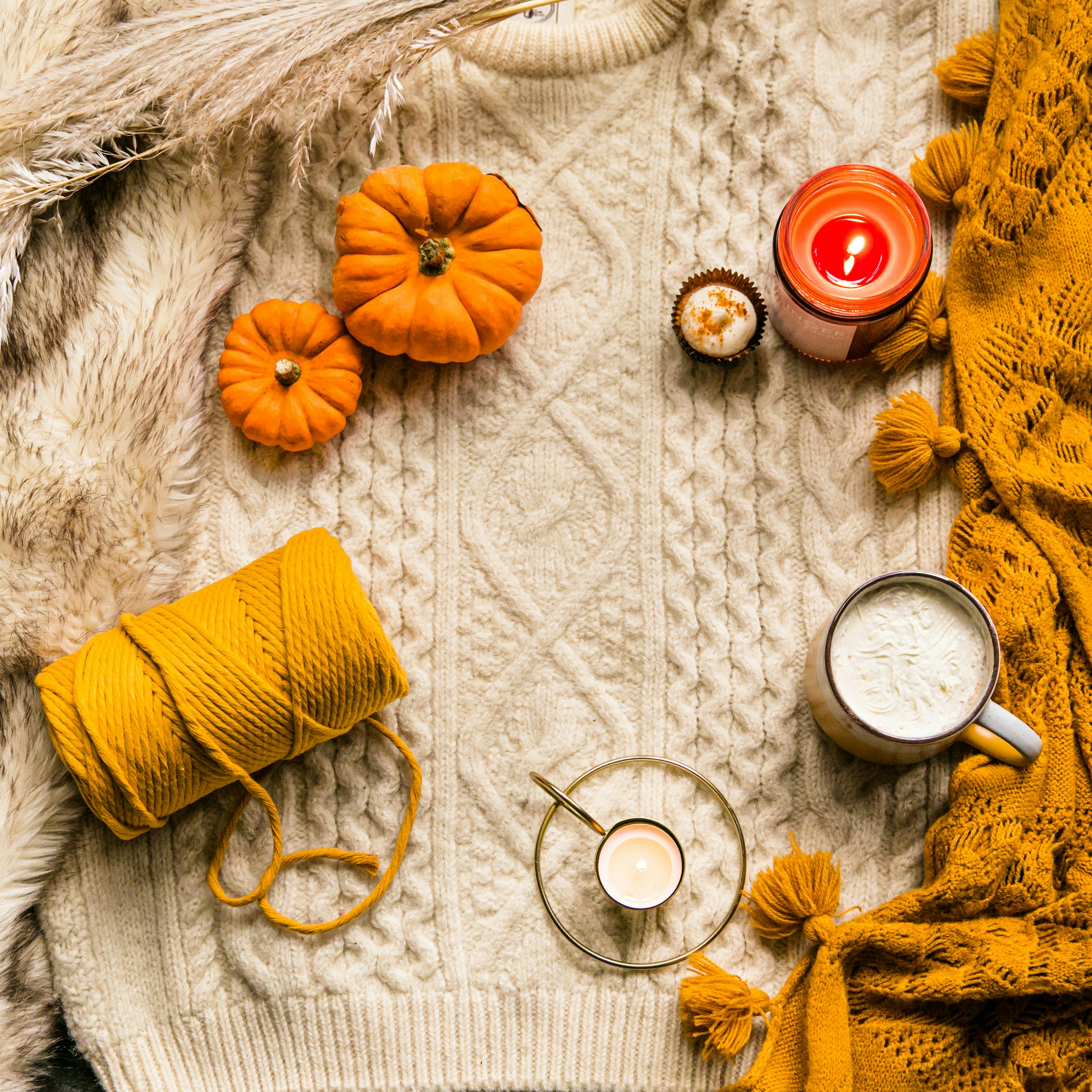 An Autumn flatlay - Candles, pumkins, mug, candles, cake and sting on a wooly jumper and a rug. Part of the Fireside in Autumn Collection.