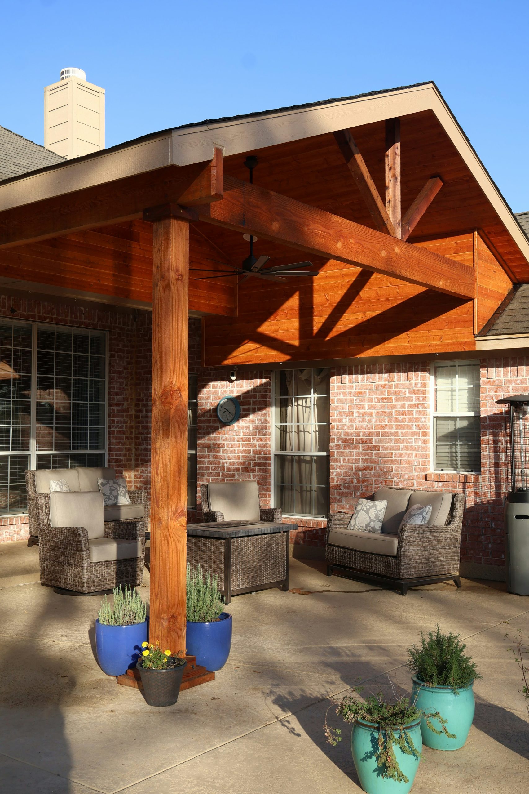 An outdoor patio with a wooden pergola and wicker furniture