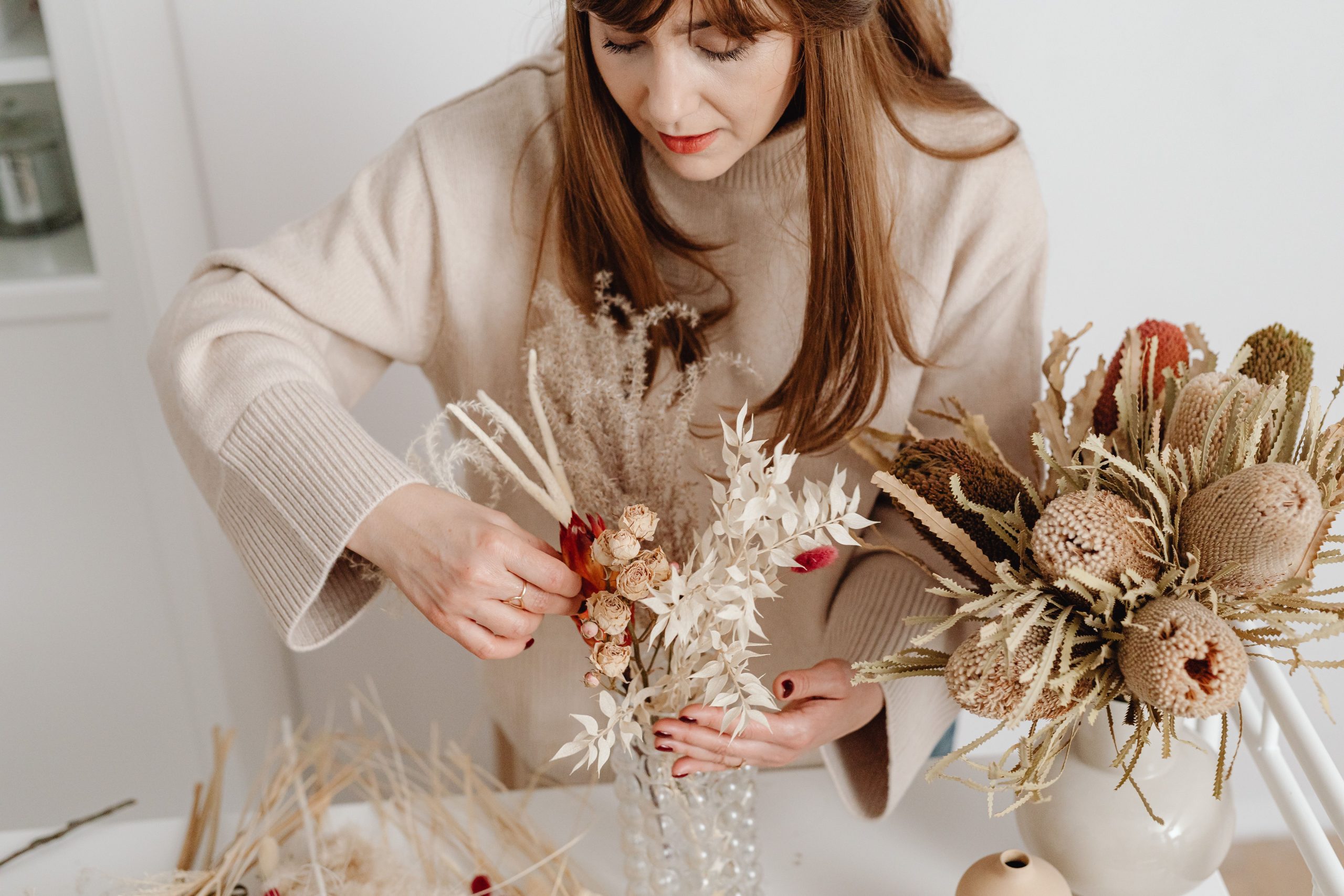 Artistic close-up of a woman arranging a sophisticated dried flower bouquet indoors.