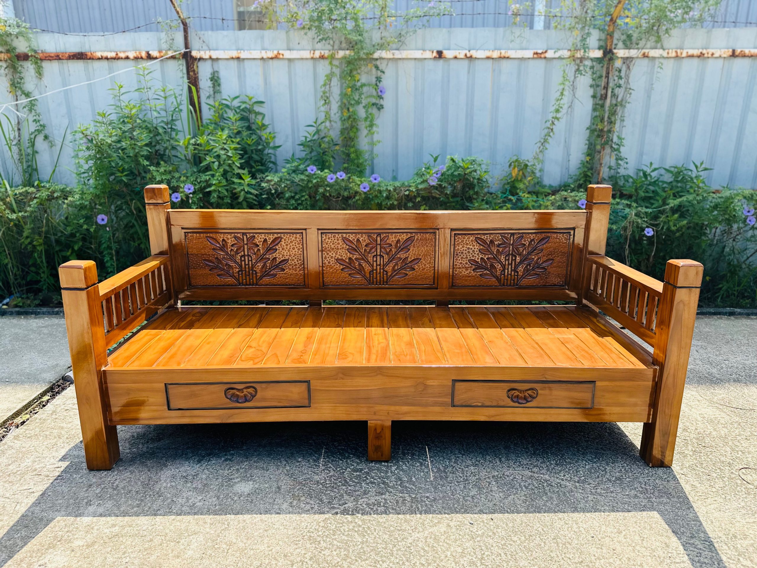 Beautiful hand-carved wooden bench with floral patterns, placed outdoors in a garden area, bathed in sunlight.